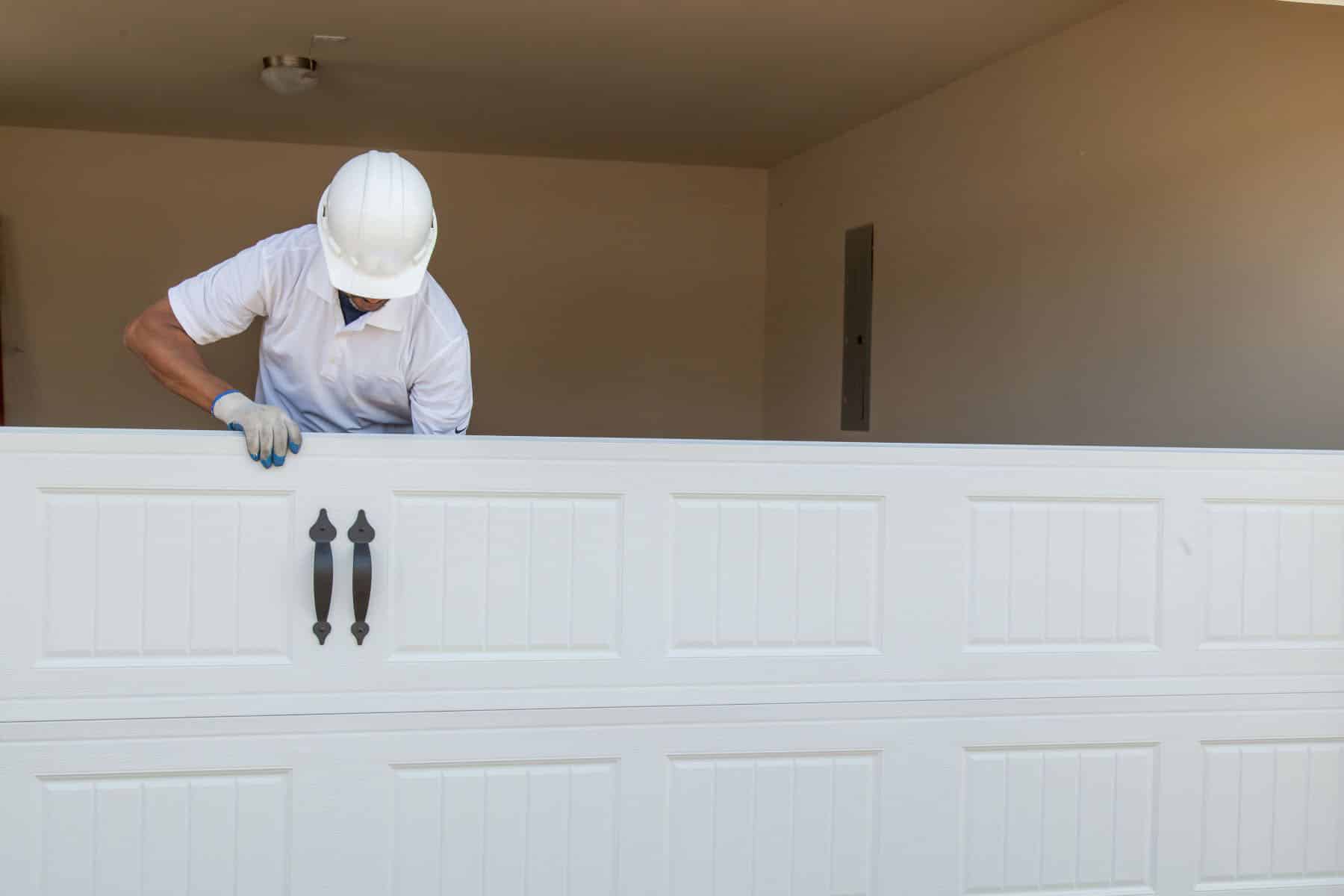 Man in hard hat installing a white garage door