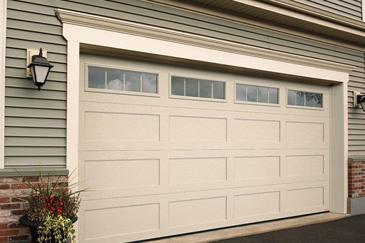 Beige garage door with windows on a house with light green siding.