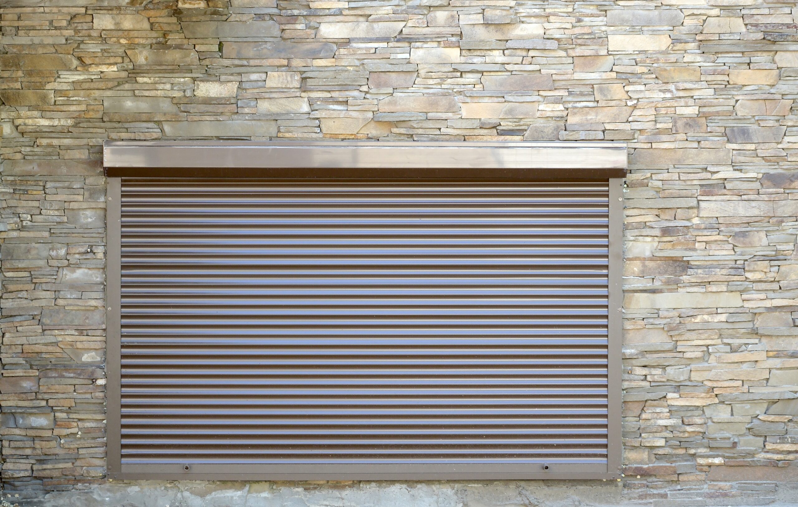 Closed brown roller shutter on a stone wall