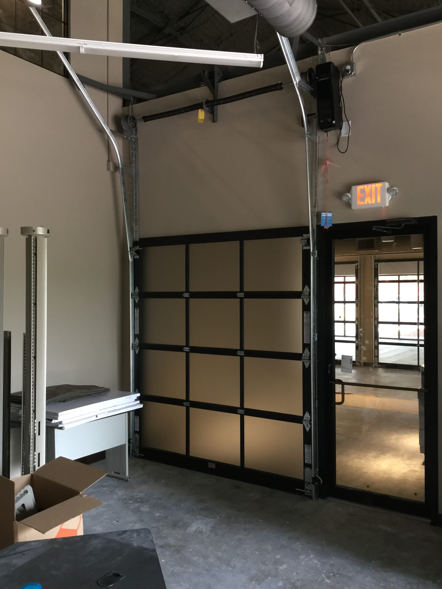 Interior view of a commercial space with a closed garage door and exit sign.