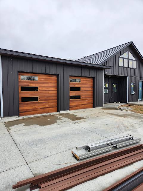 Two modern wooden garage doors on a dark gray building with a concrete driveway.