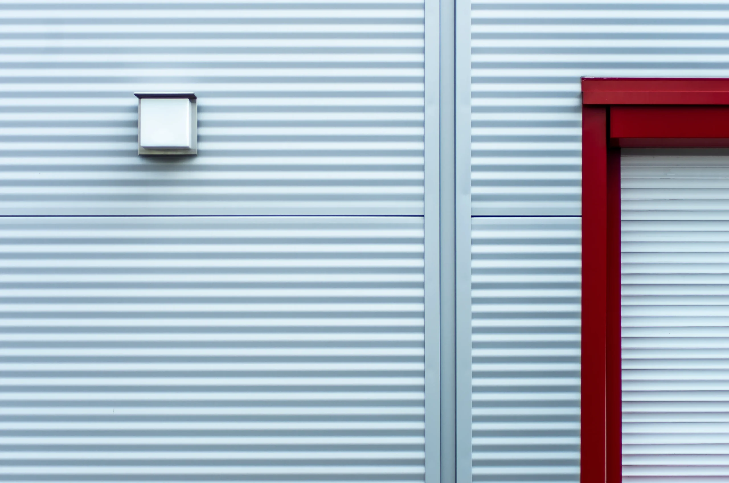Corrugated metal wall with a white light fixture and a red door frame.