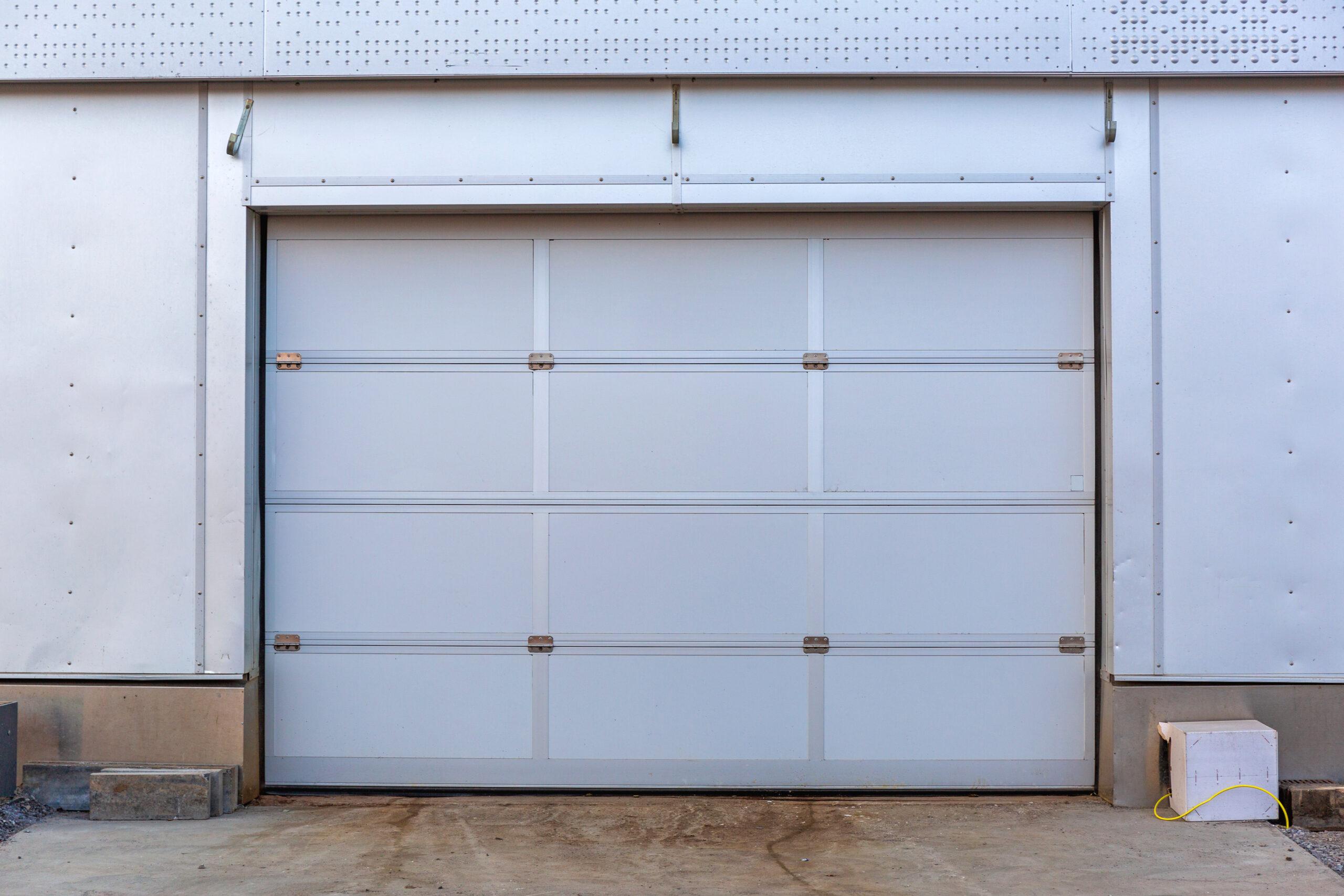 Closed white garage door on a building with metal siding