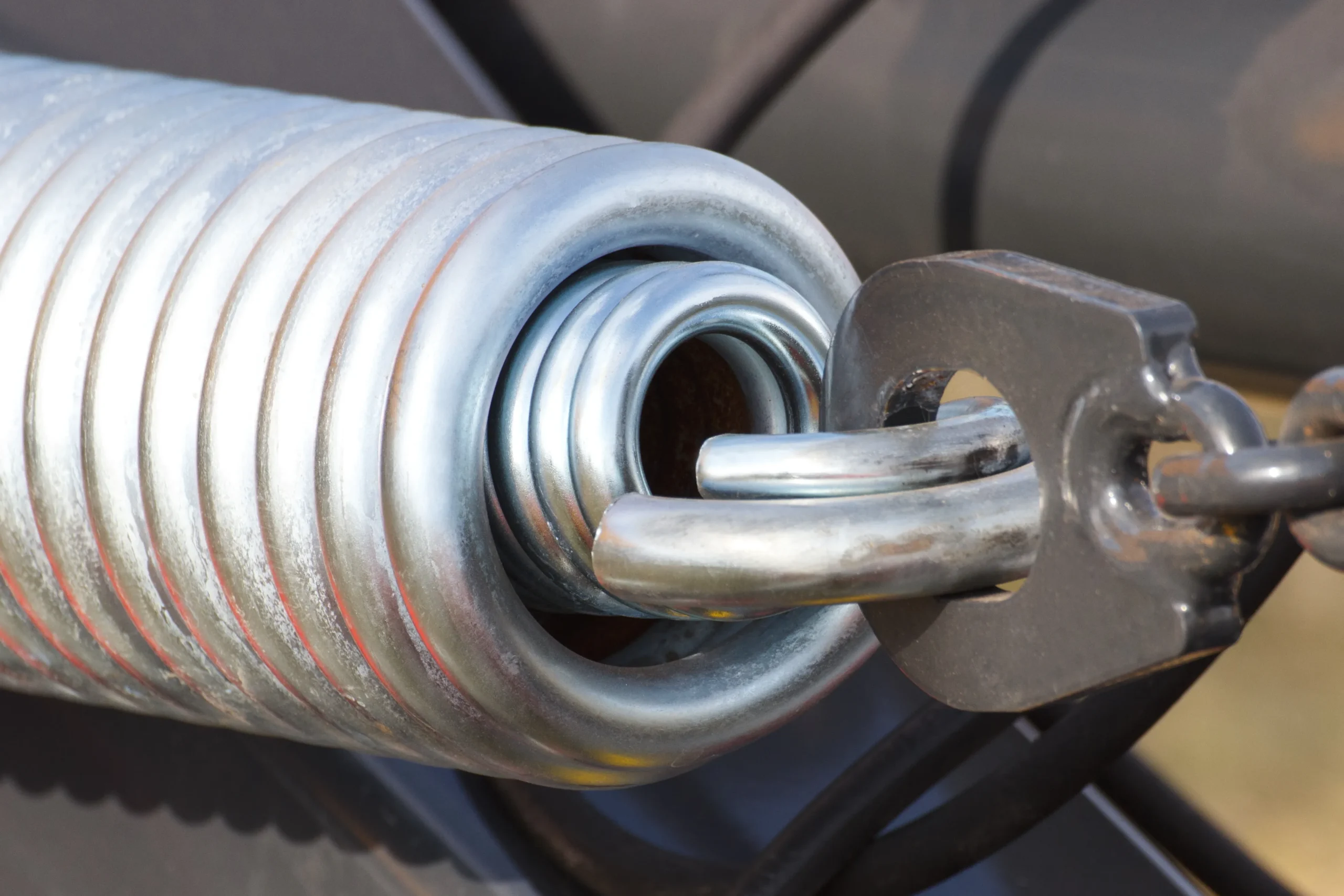 Close-up of a large metal spring with a chain link attached.