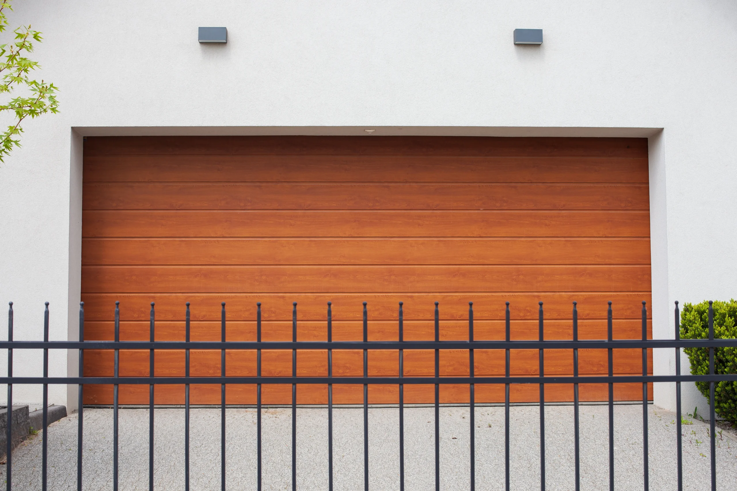Modern garage door with wooden panels behind a black metal fence.