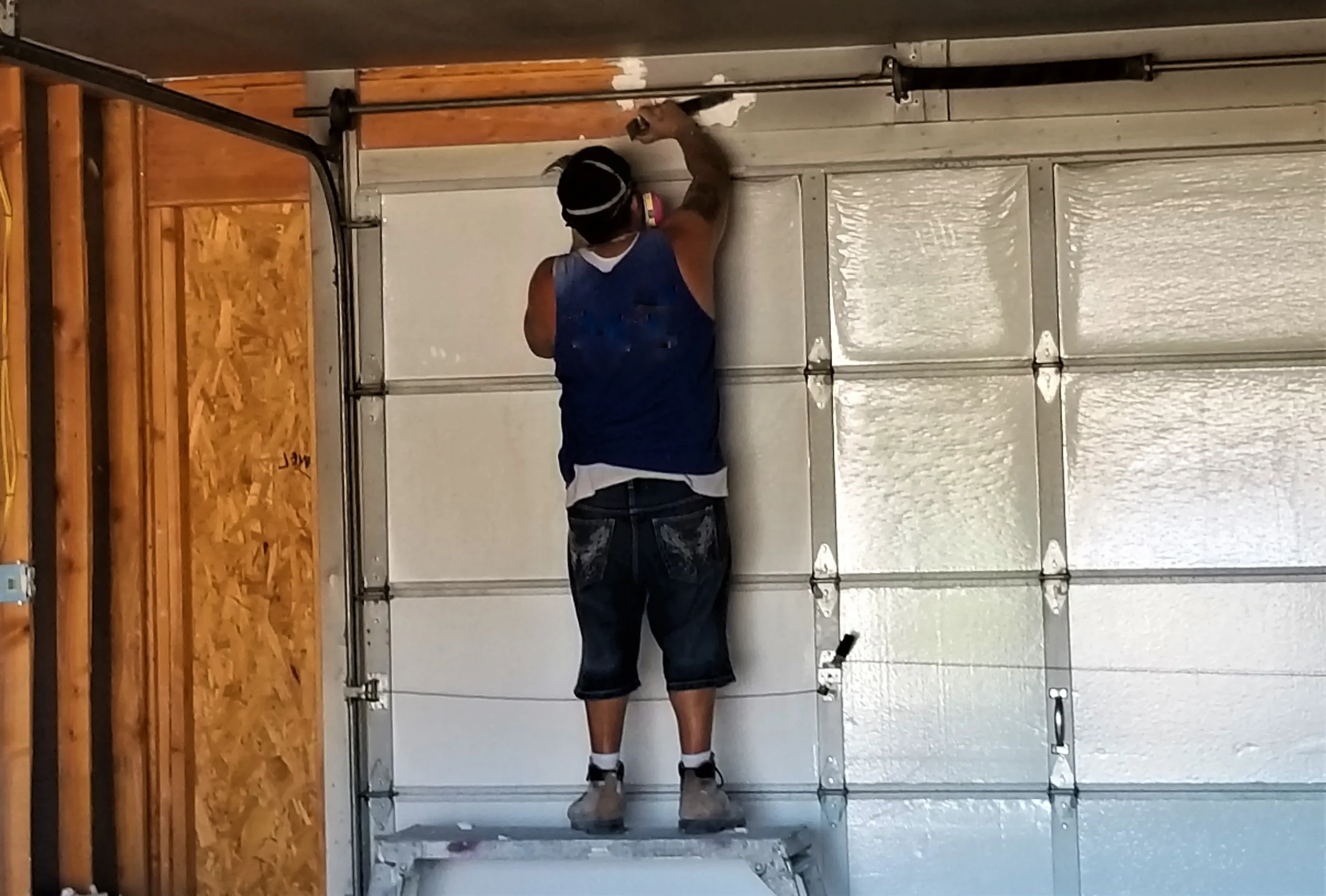 Man on a ladder repairing a white garage door.