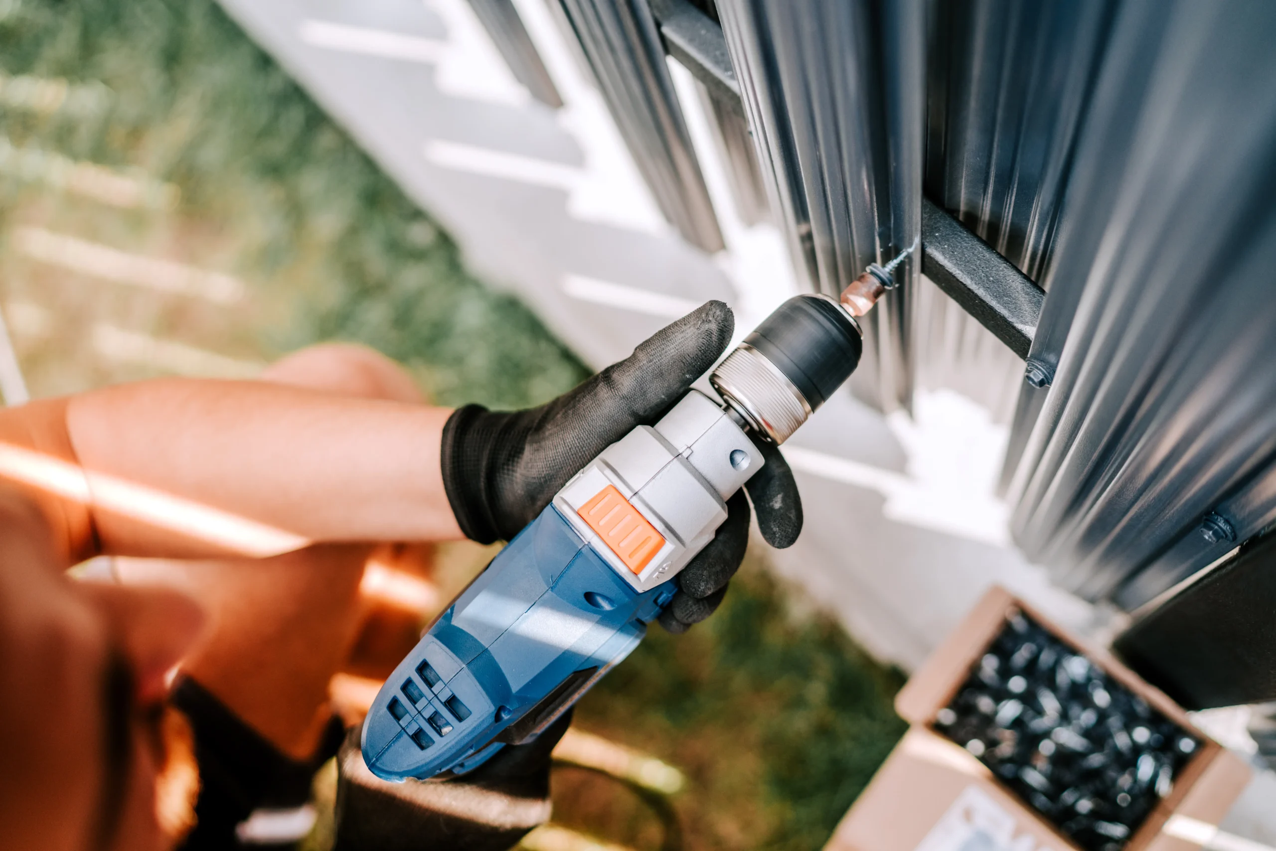 Person using a blue and white drill on a dark metal fence