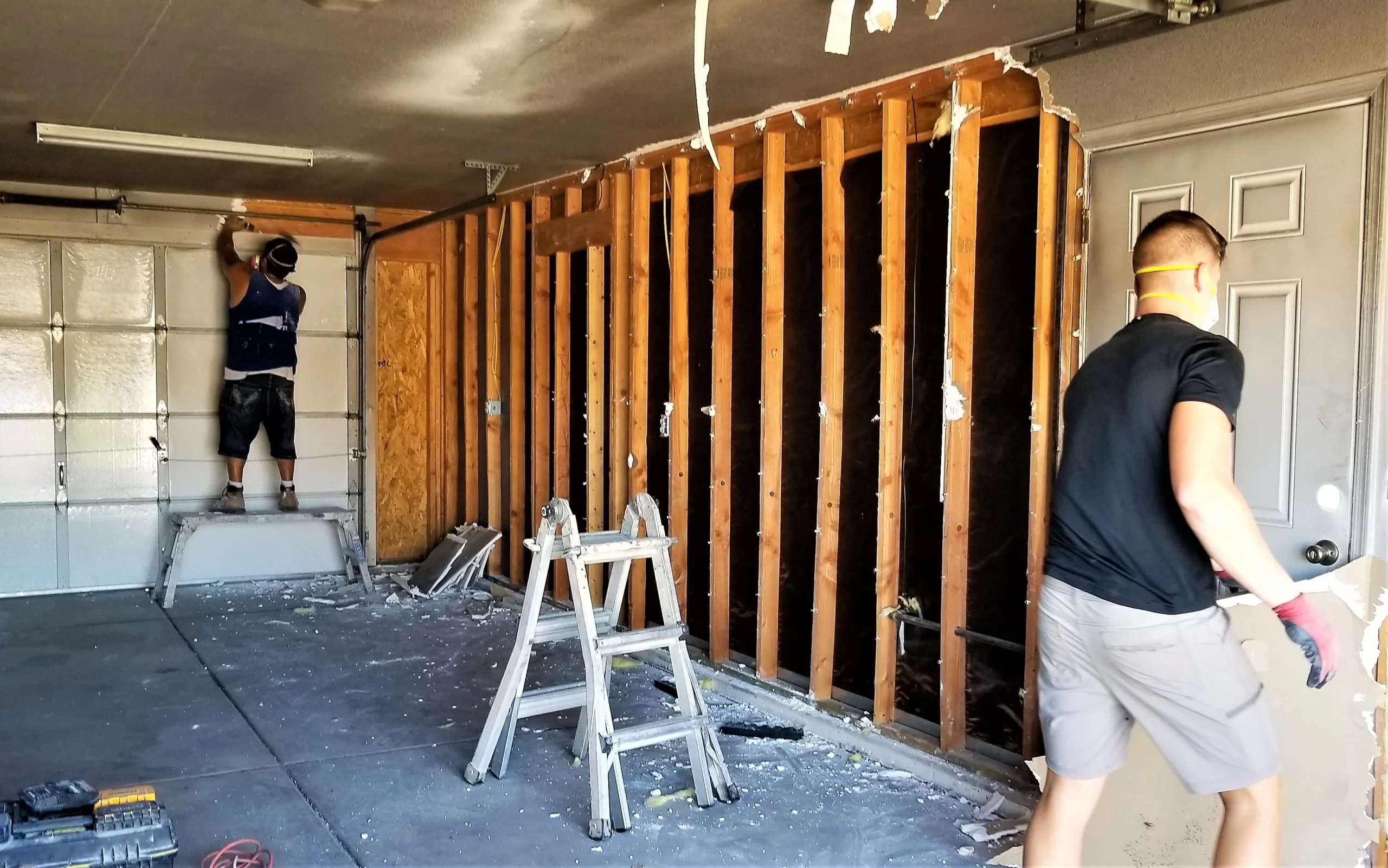 Two men working on a garage renovation with exposed wooden studs.