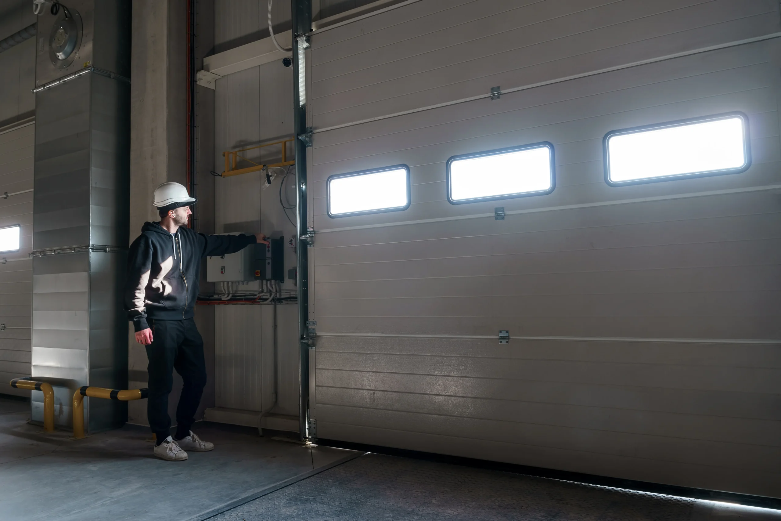Man in hard hat operating a large garage door in a warehouse.