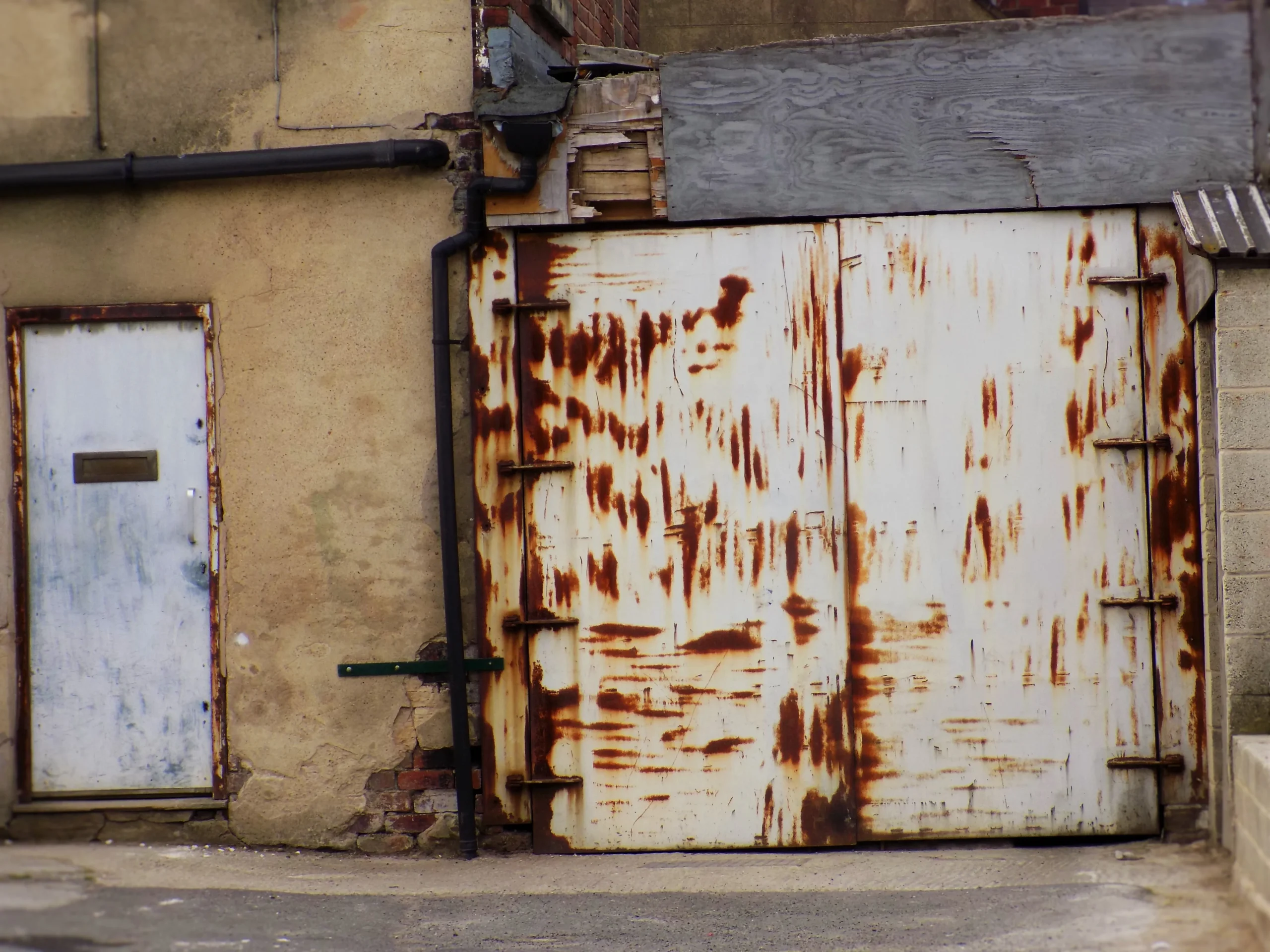 Weathered white door and rusty metal garage door on an old building