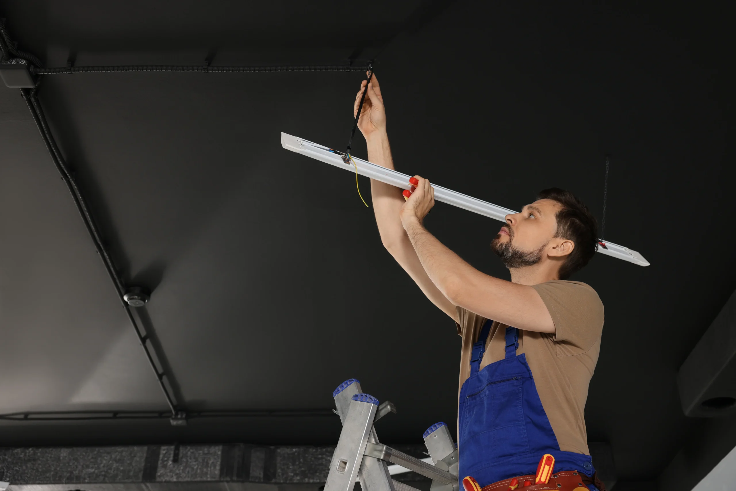 Man installing fluorescent light fixture on a dark ceiling