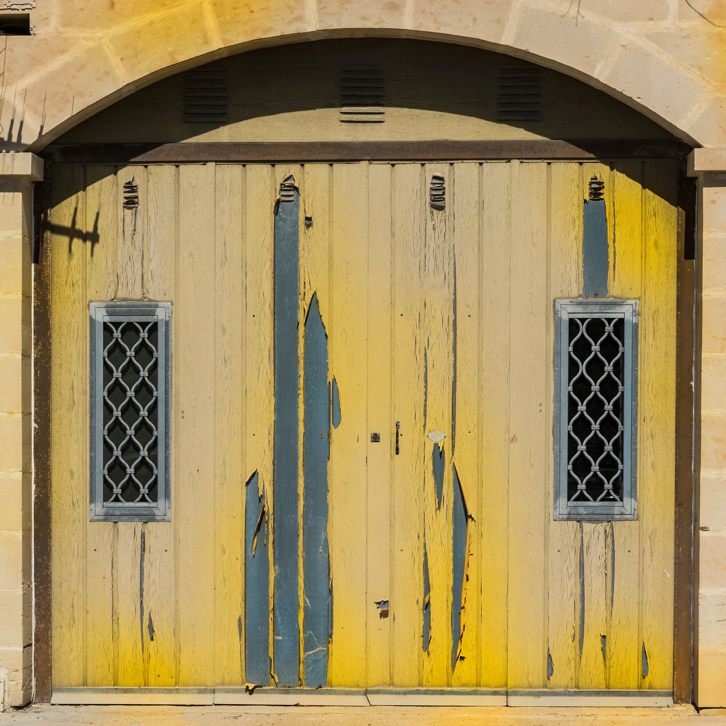 Weathered yellow wooden door with peeling paint and two barred windows