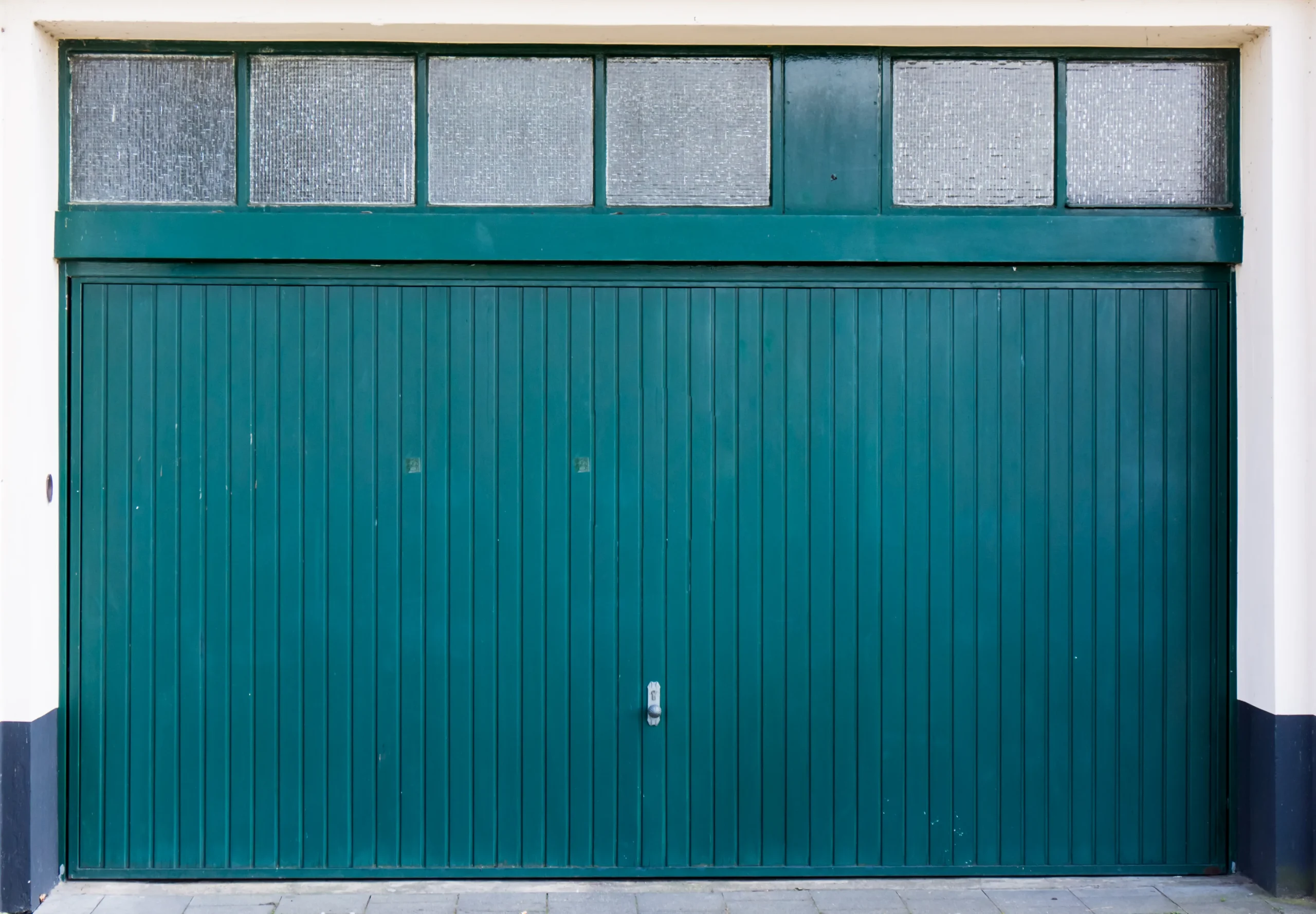 A teal garage door with small frosted windows above it.