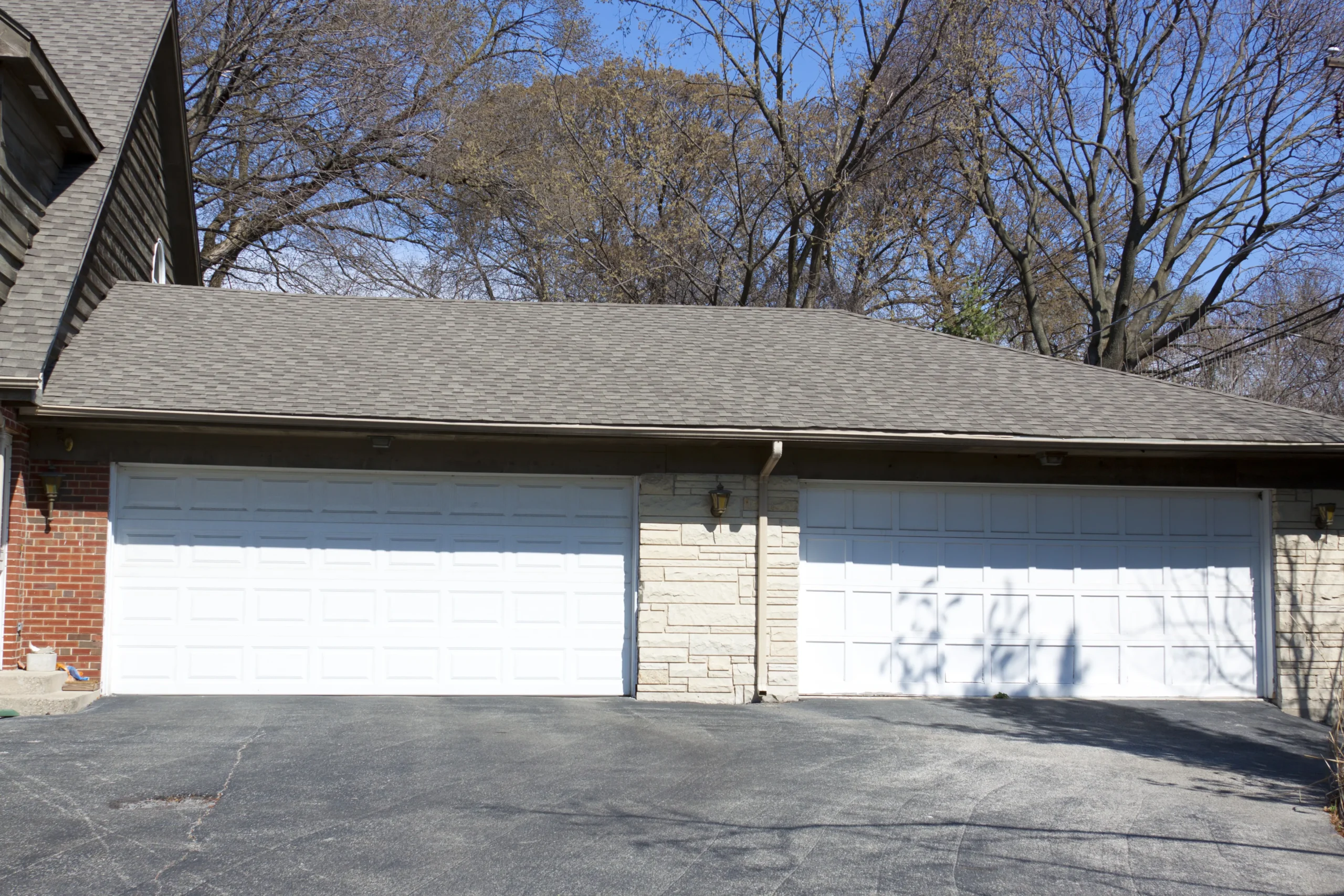 Two white garage doors on a house with a gray roof and brick siding.