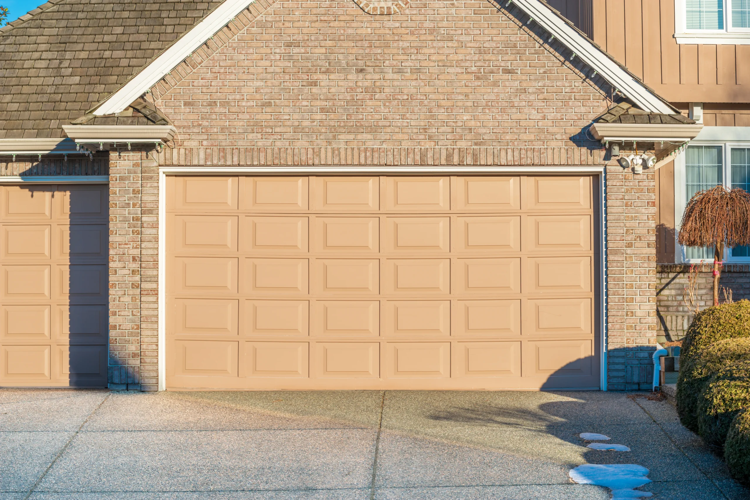 Two beige garage doors on a brick house with a concrete driveway