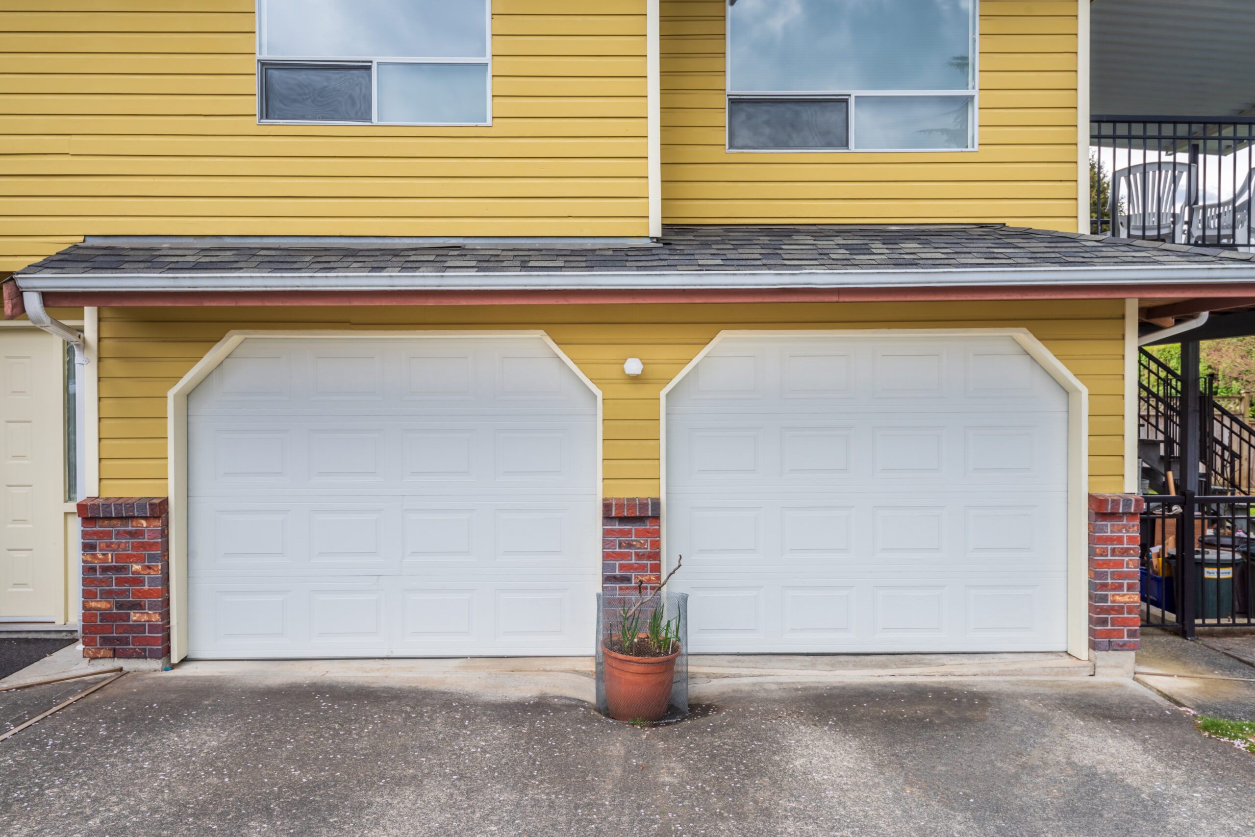 Two white garage doors on a yellow house with brick accents