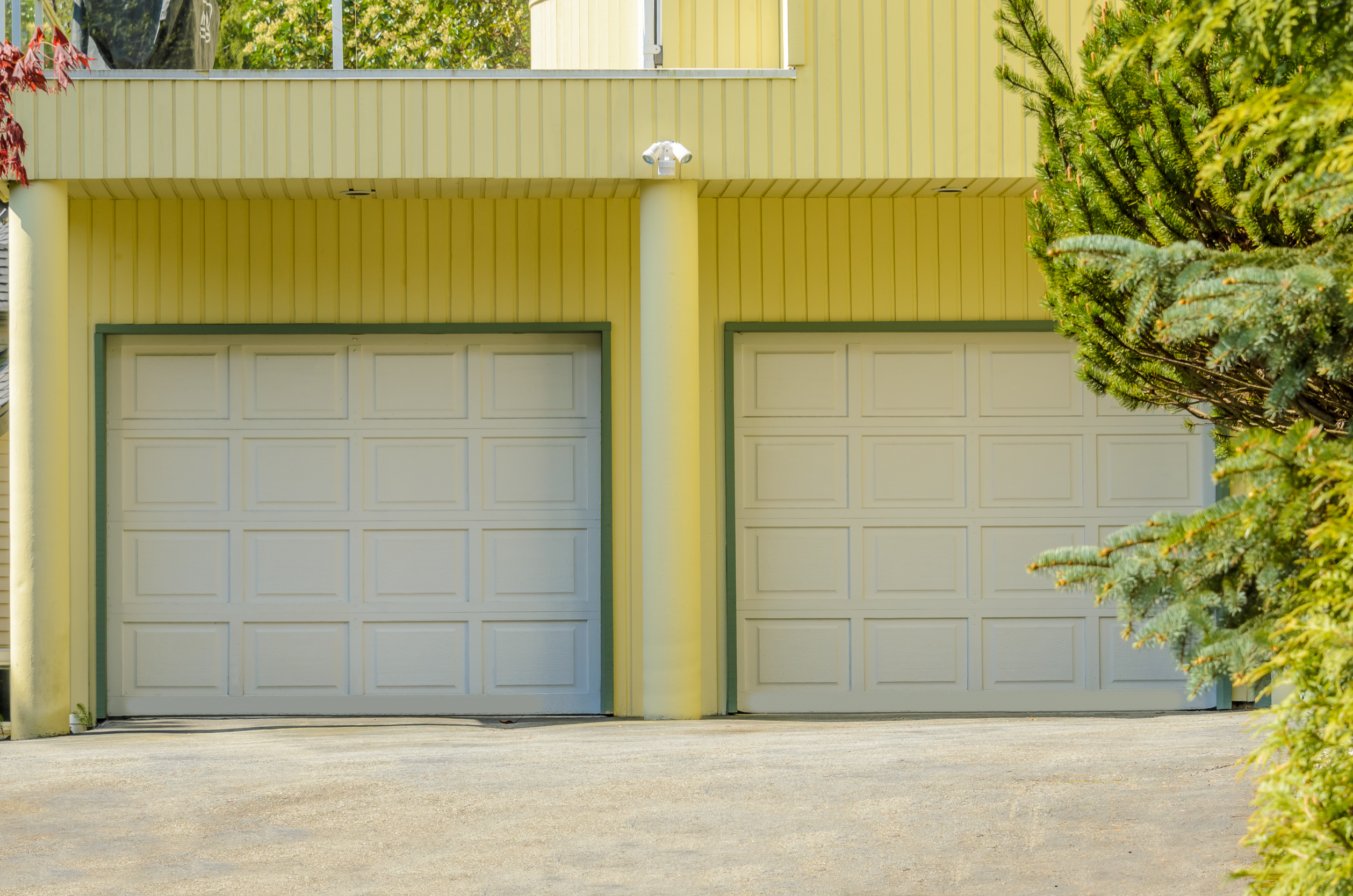 Two white garage doors on a yellow house with green trim and a driveway.