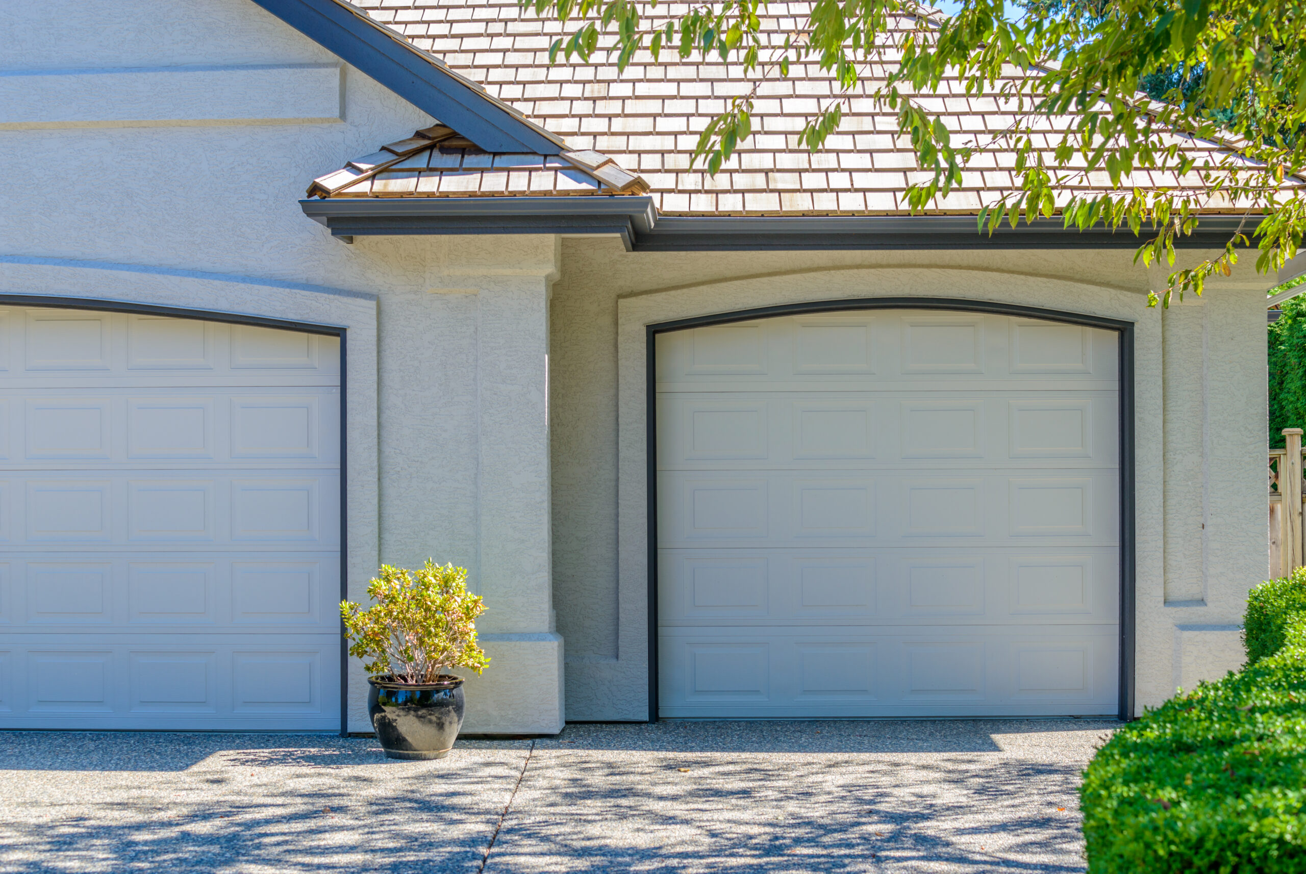 Two white garage doors on a house with a tiled roof and green foliage.