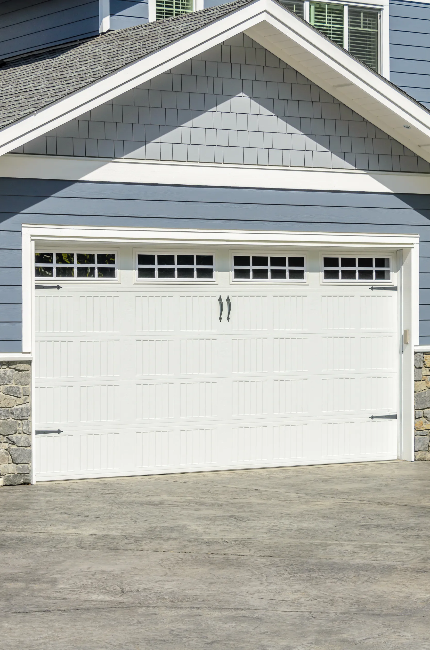 White garage door with windows on a blue house with stone accents.