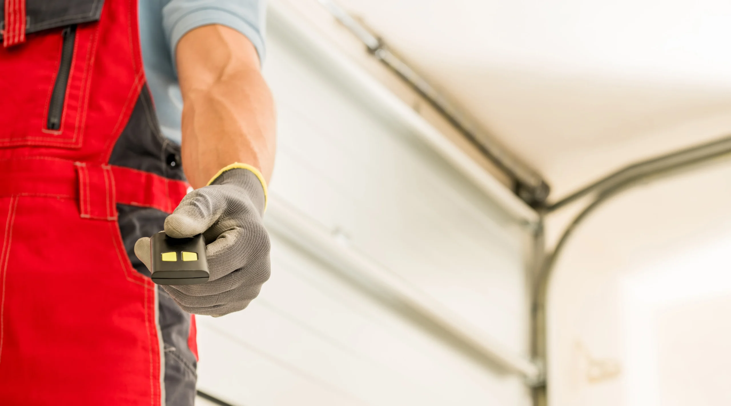 Person in red overalls and glove holding a garage door opener.