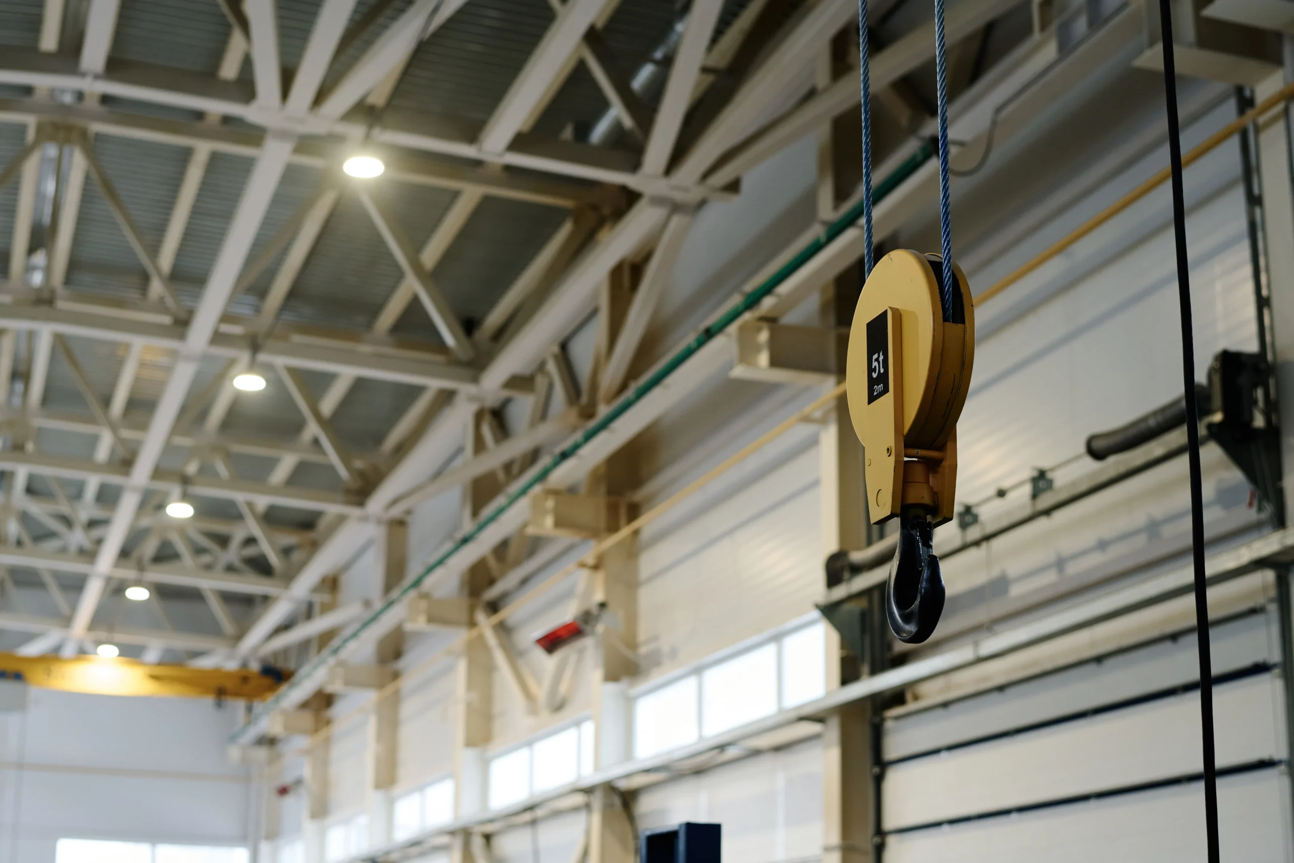 Yellow crane hook and pulley system in a large industrial building.