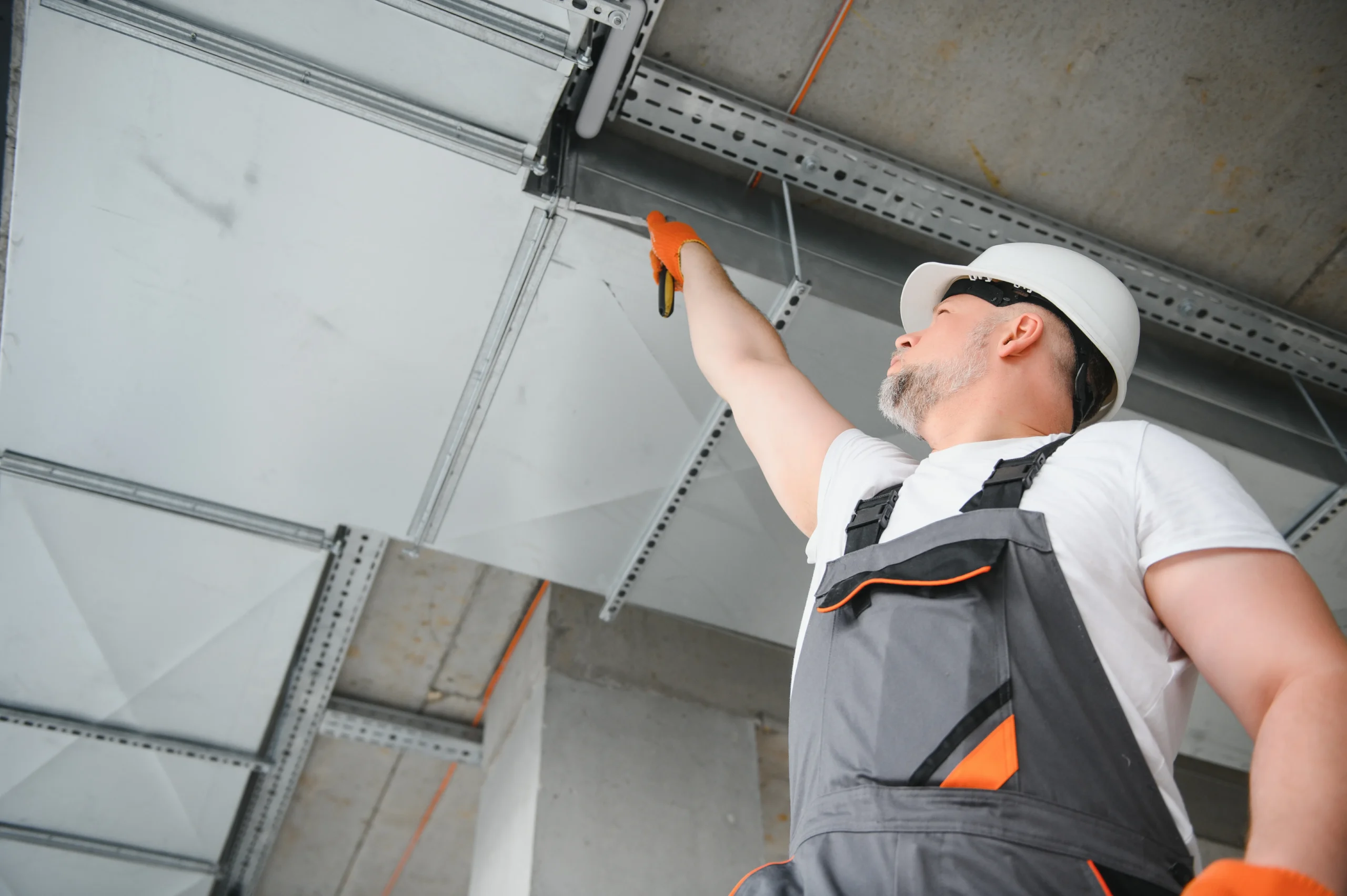 Man in hard hat and work clothes installing ceiling panels.