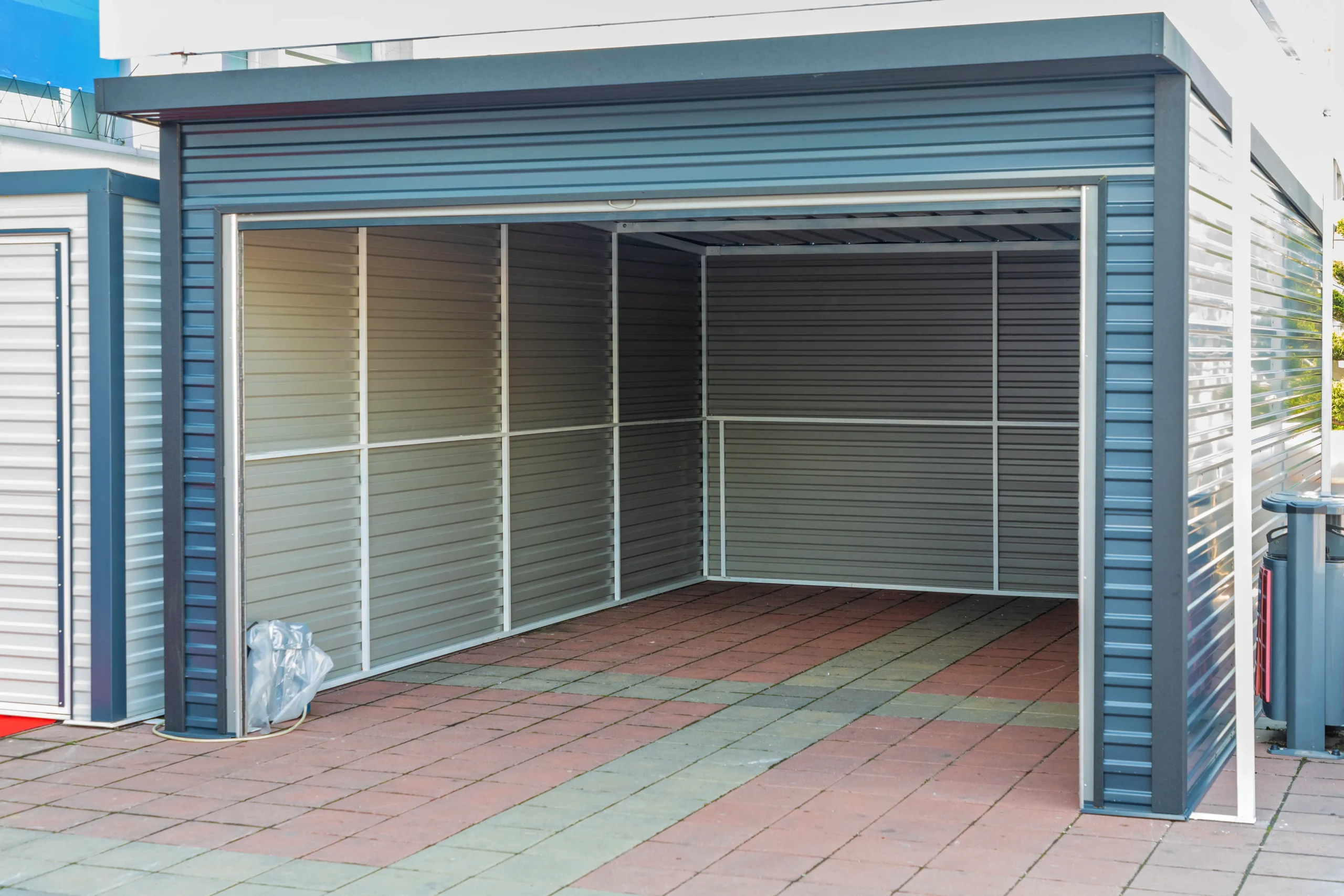Empty metal garage with an open roller door and a paved floor