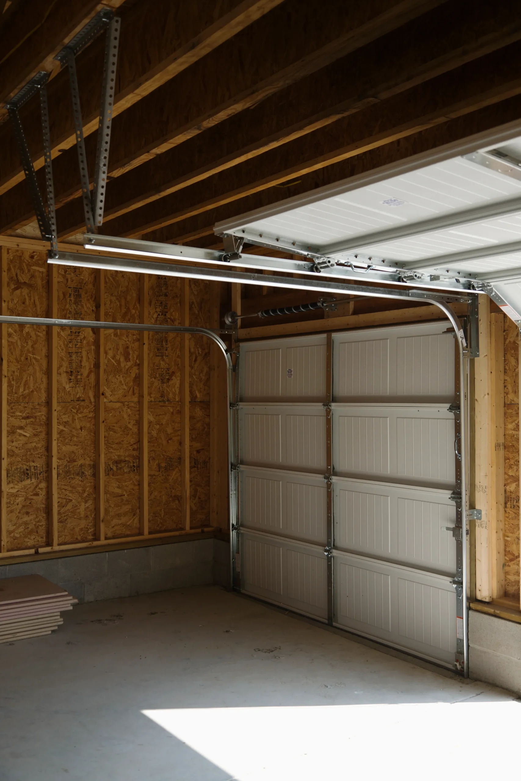Interior view of an unfinished garage with a white open garage door.