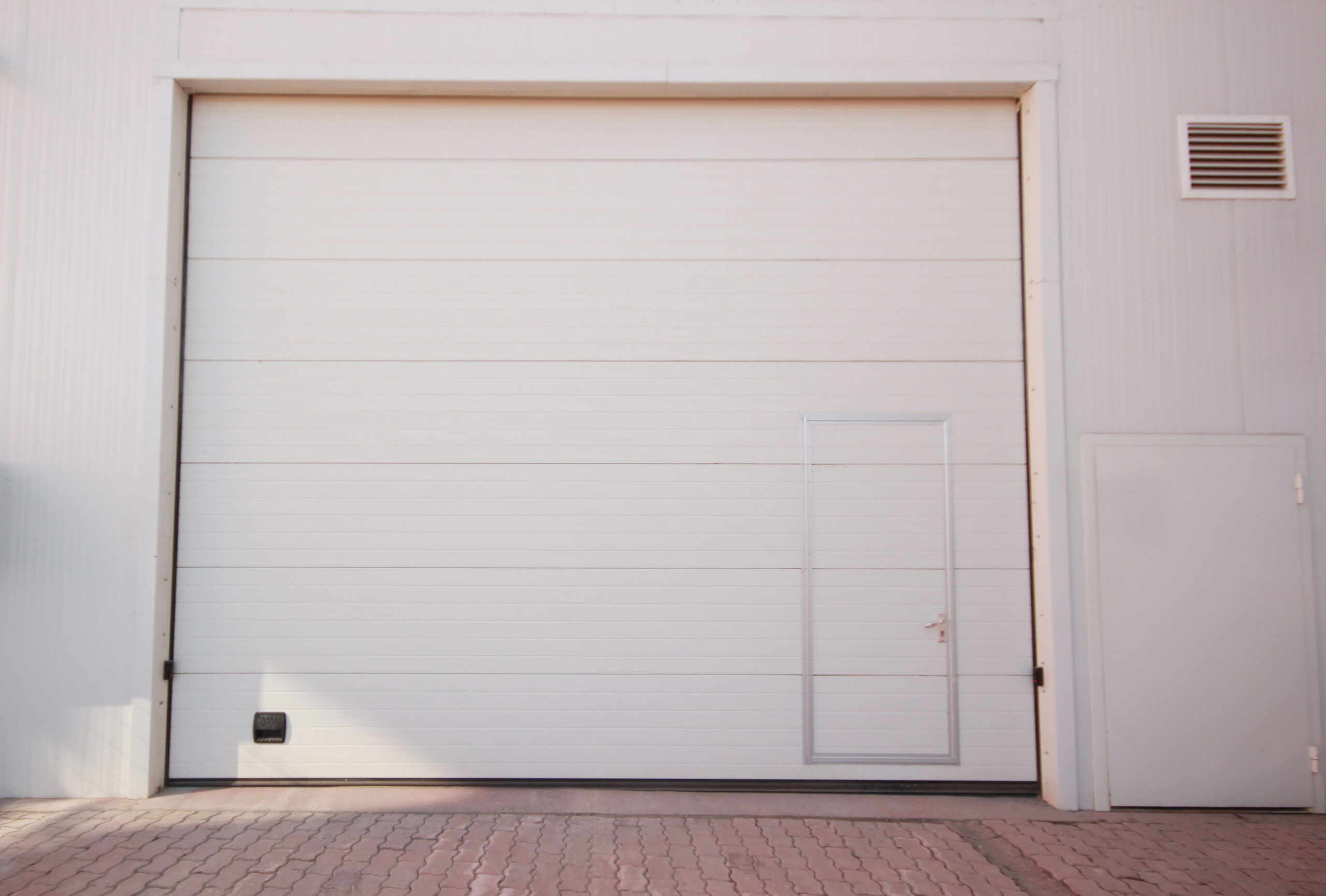 Large white garage door with a smaller door, on a building with a vent