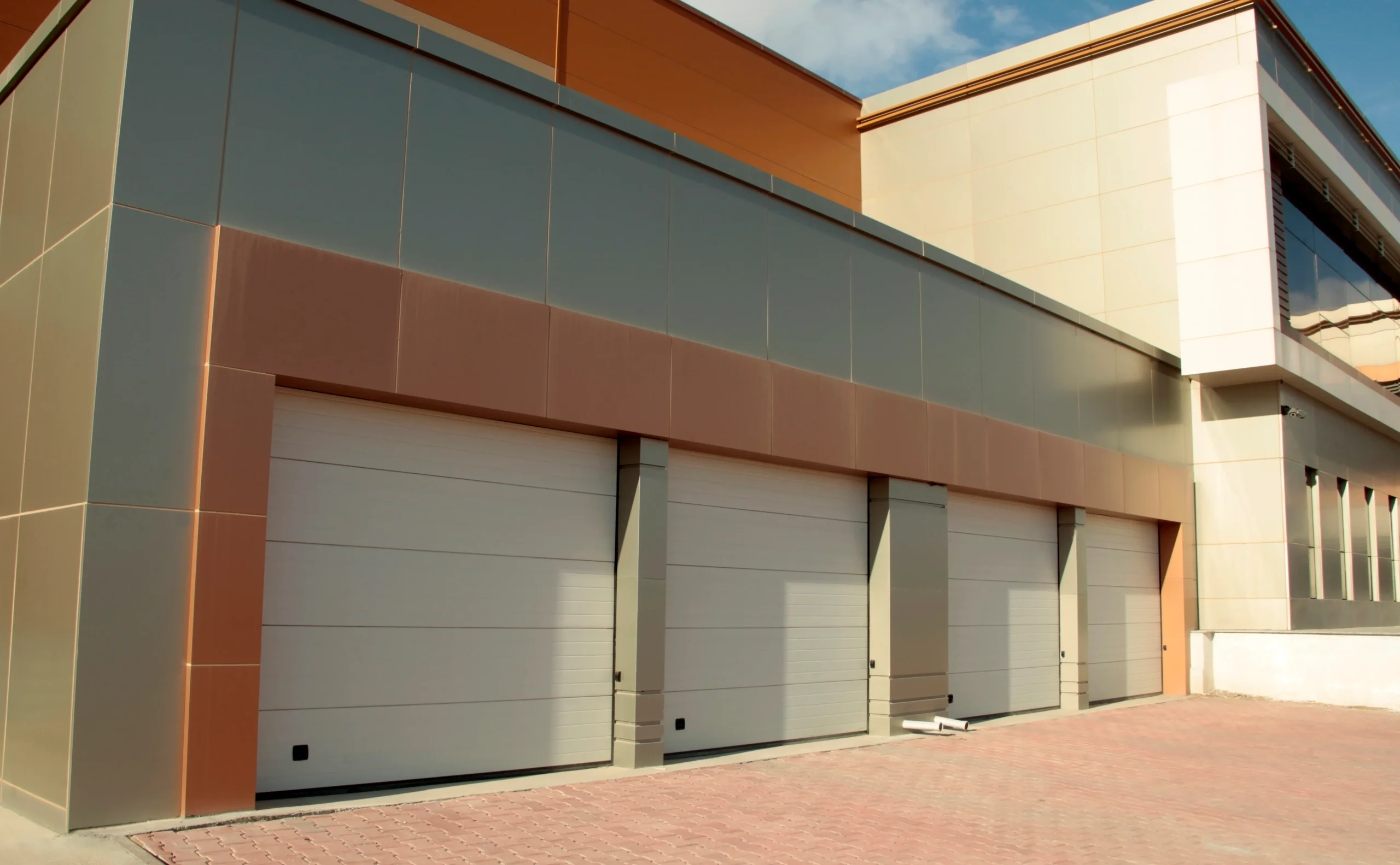 Modern building with multiple garage doors and a brick pavement.