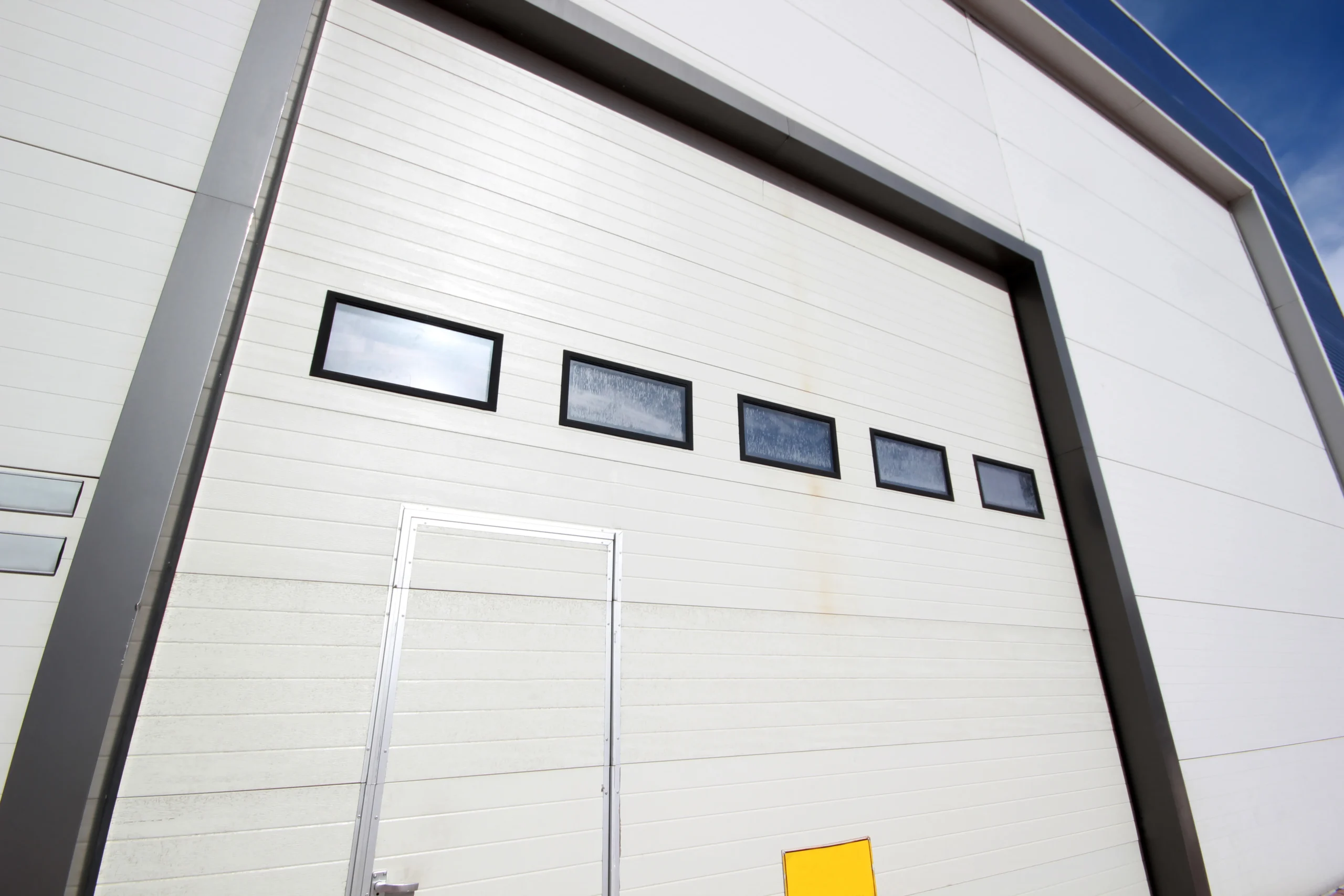 White industrial building with large garage door and small windows.