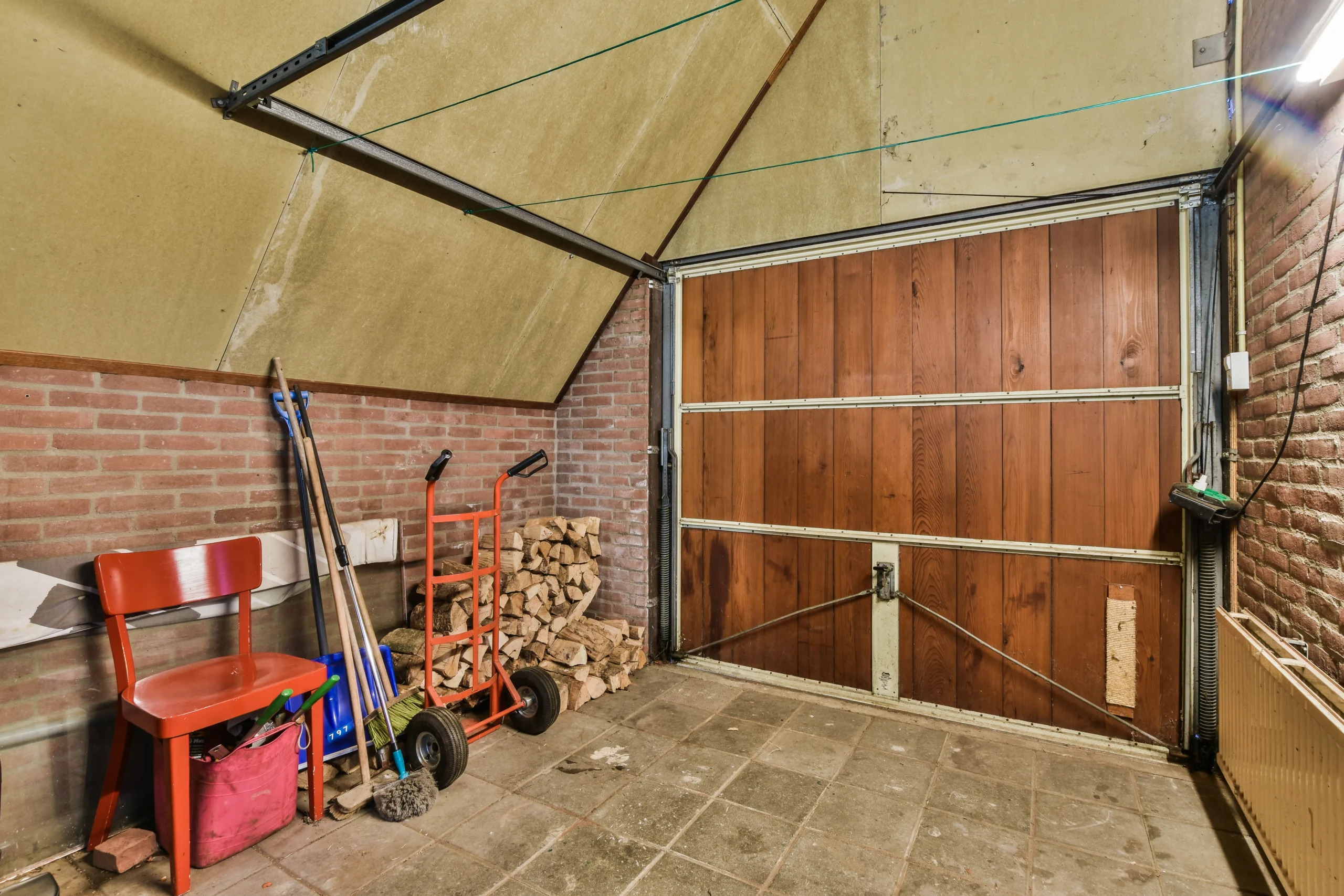 Messy garage interior with a wooden door, brick walls, and various items.