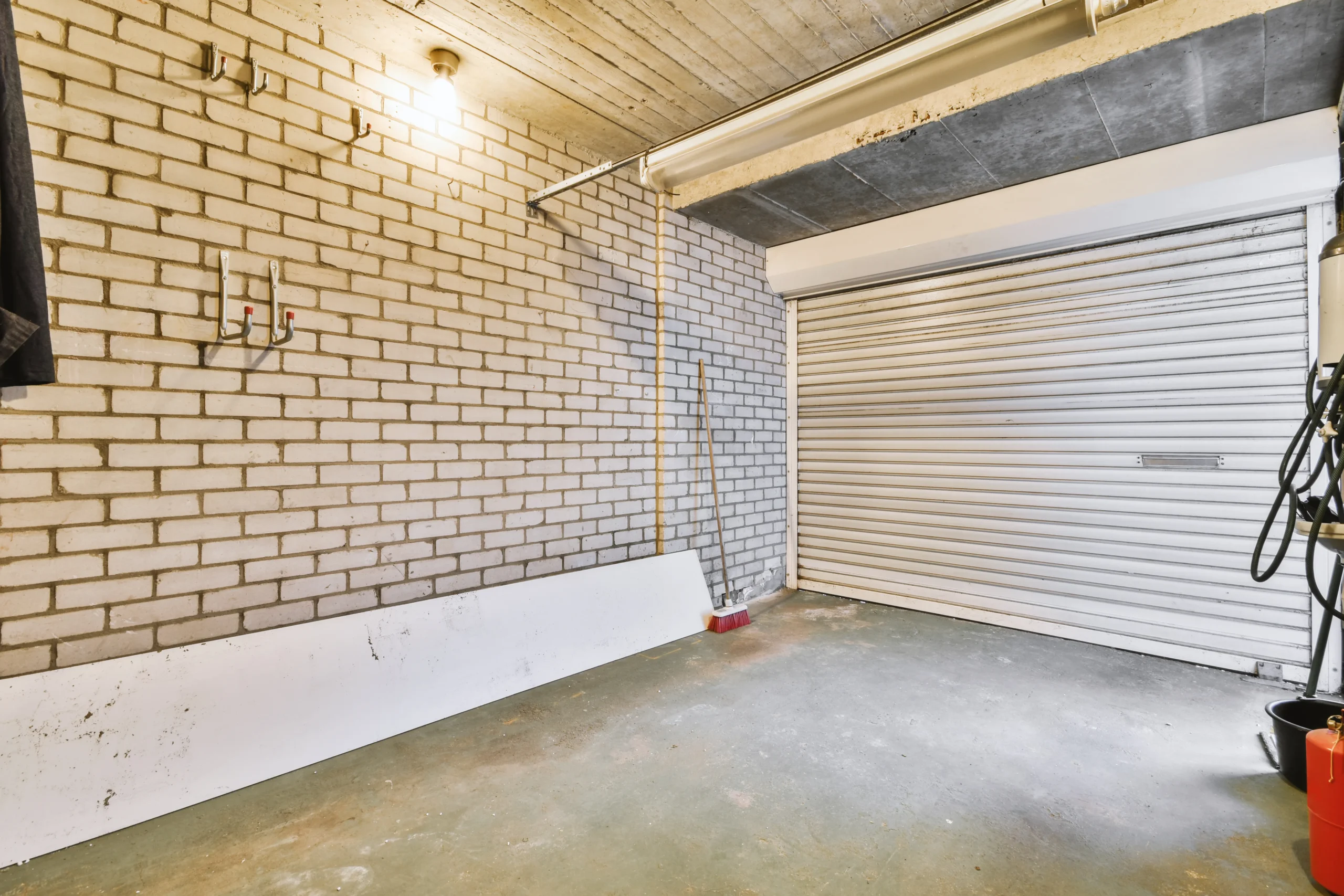 Empty garage with white brick walls, concrete ceiling, and a closed roller door.