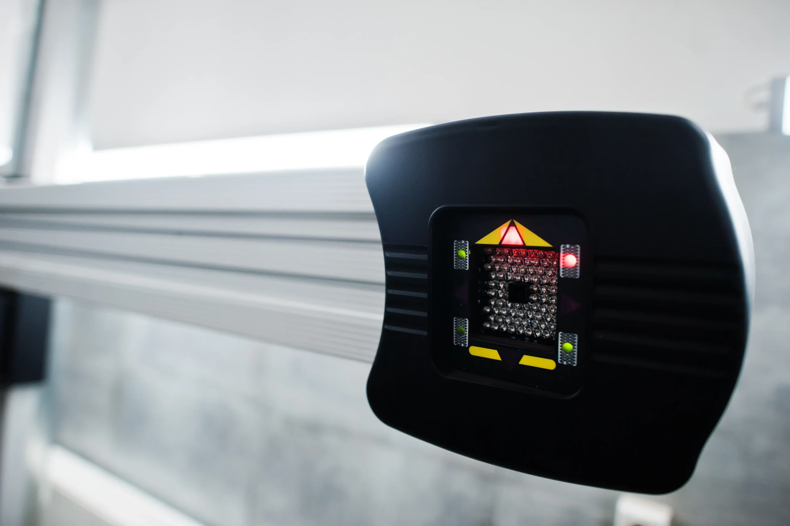 Close-up of a black sensor with red and green lights on a metal bar.
