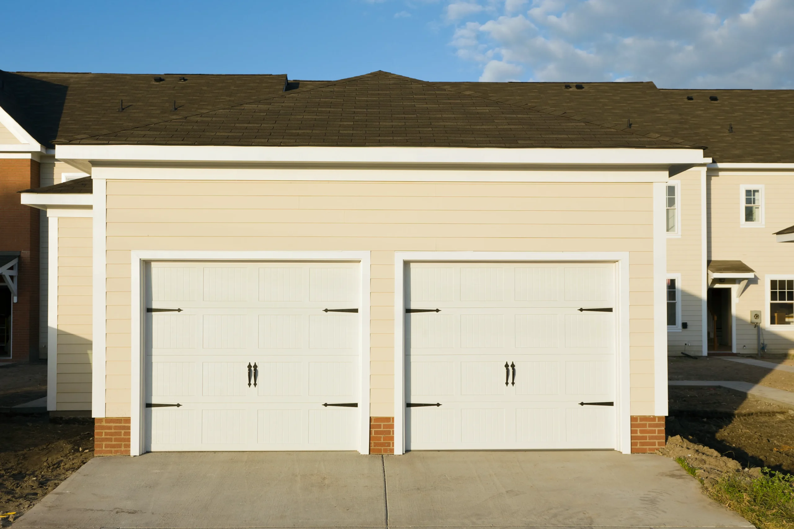 Two white garage doors on a light yellow house with a brown roof.