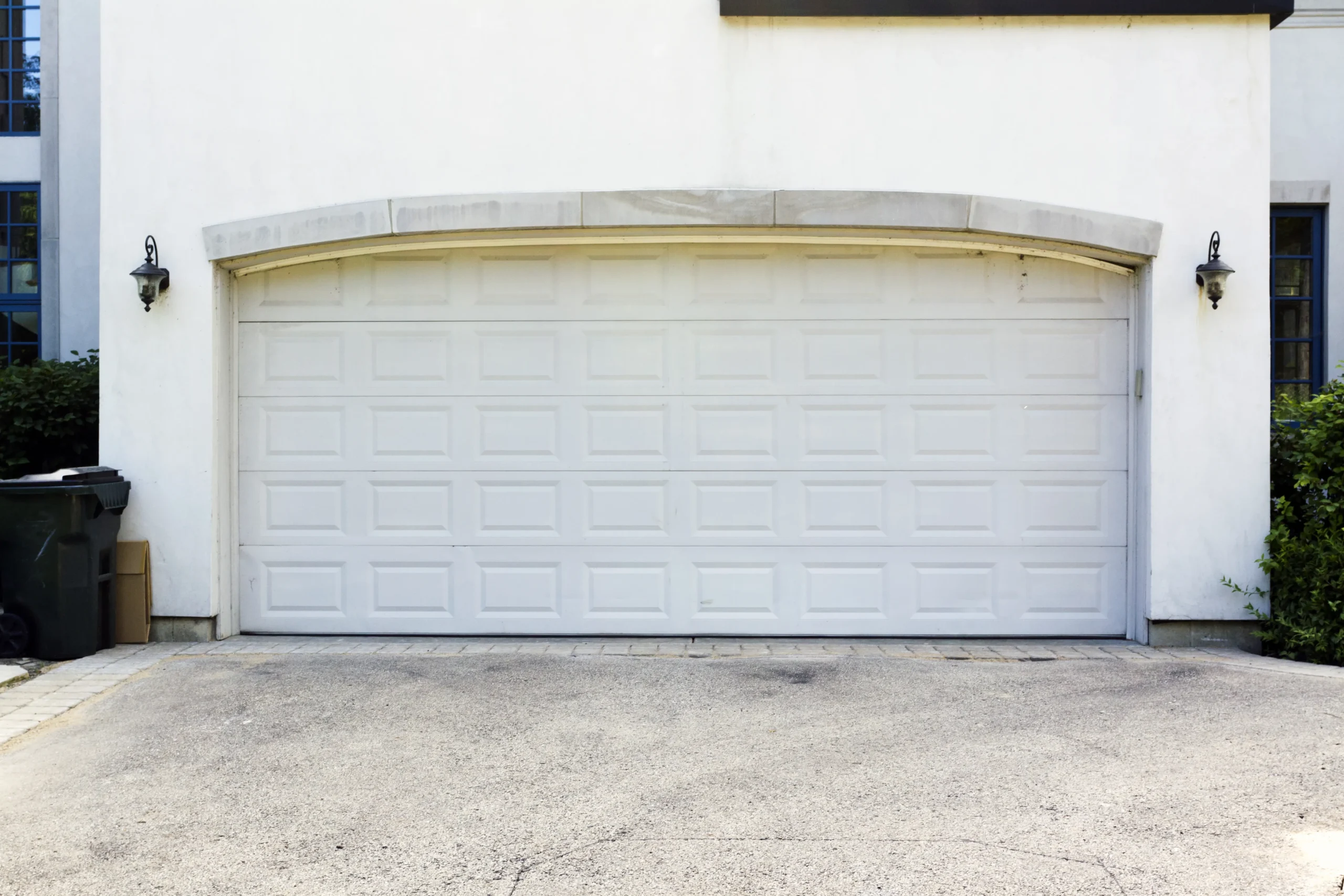 White garage door on a house with two black lanterns and a driveway.