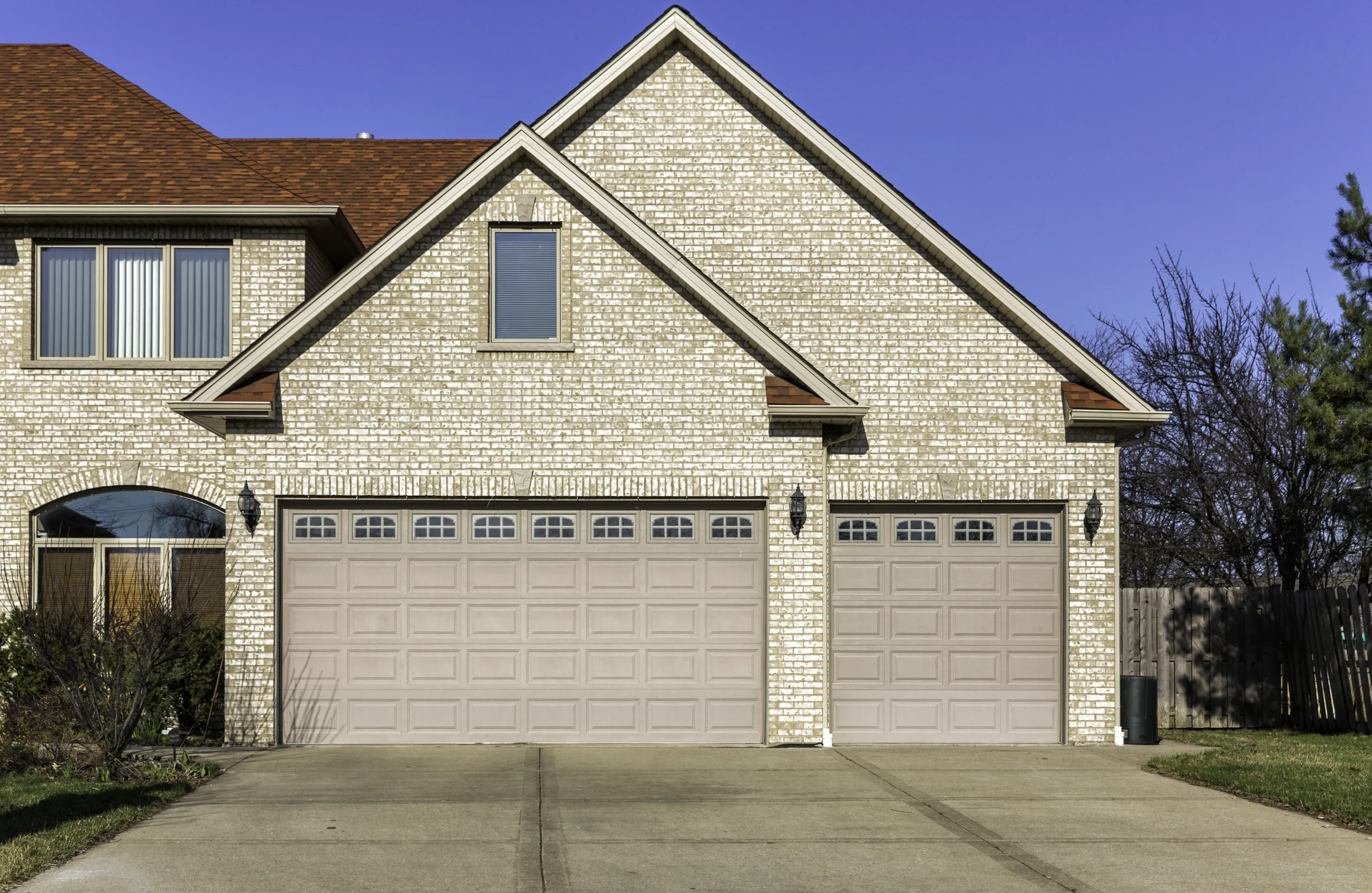 Two-story house with light brick, two garage doors, and a red roof.