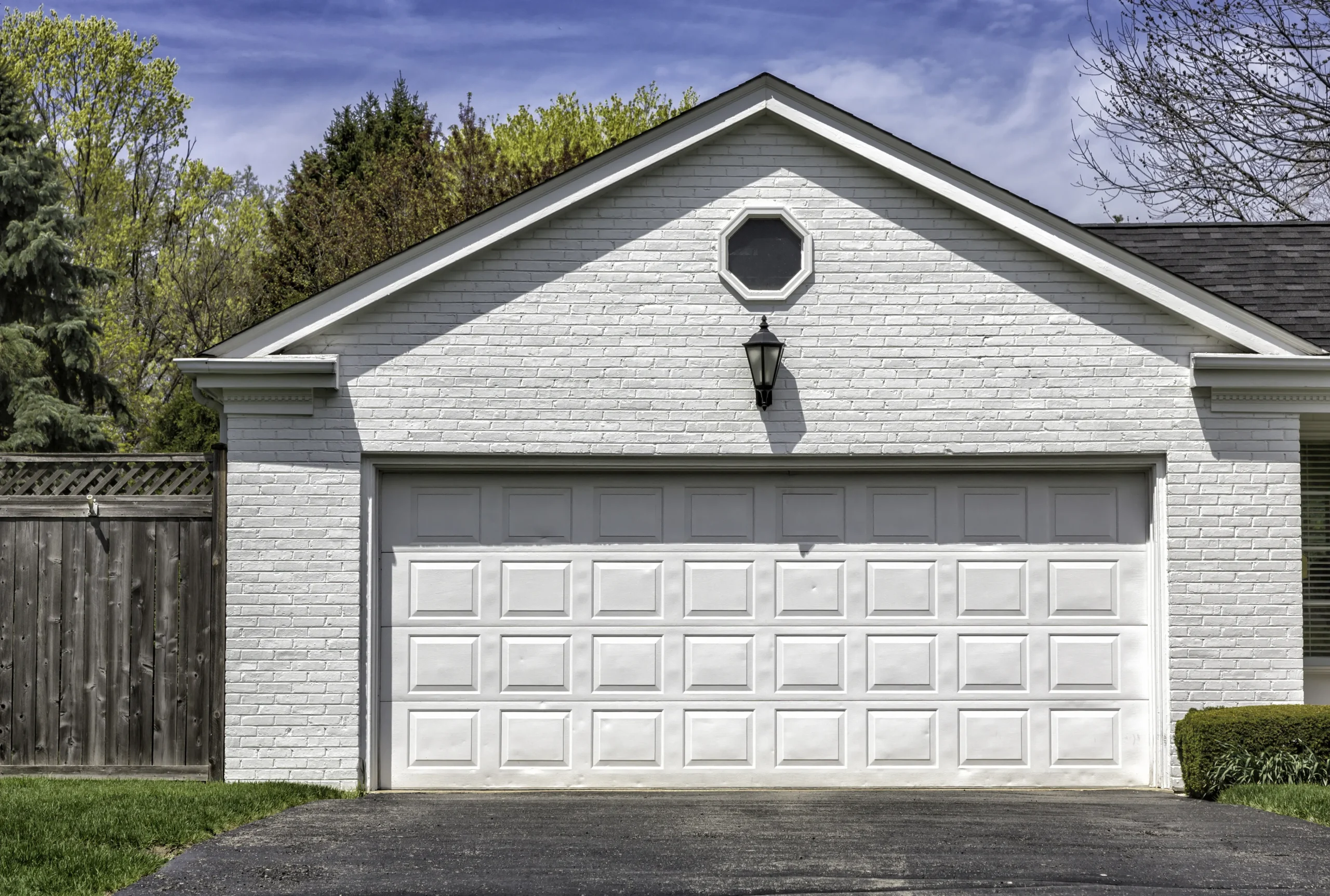 White brick garage with a single door, octagonal window, and black lantern.