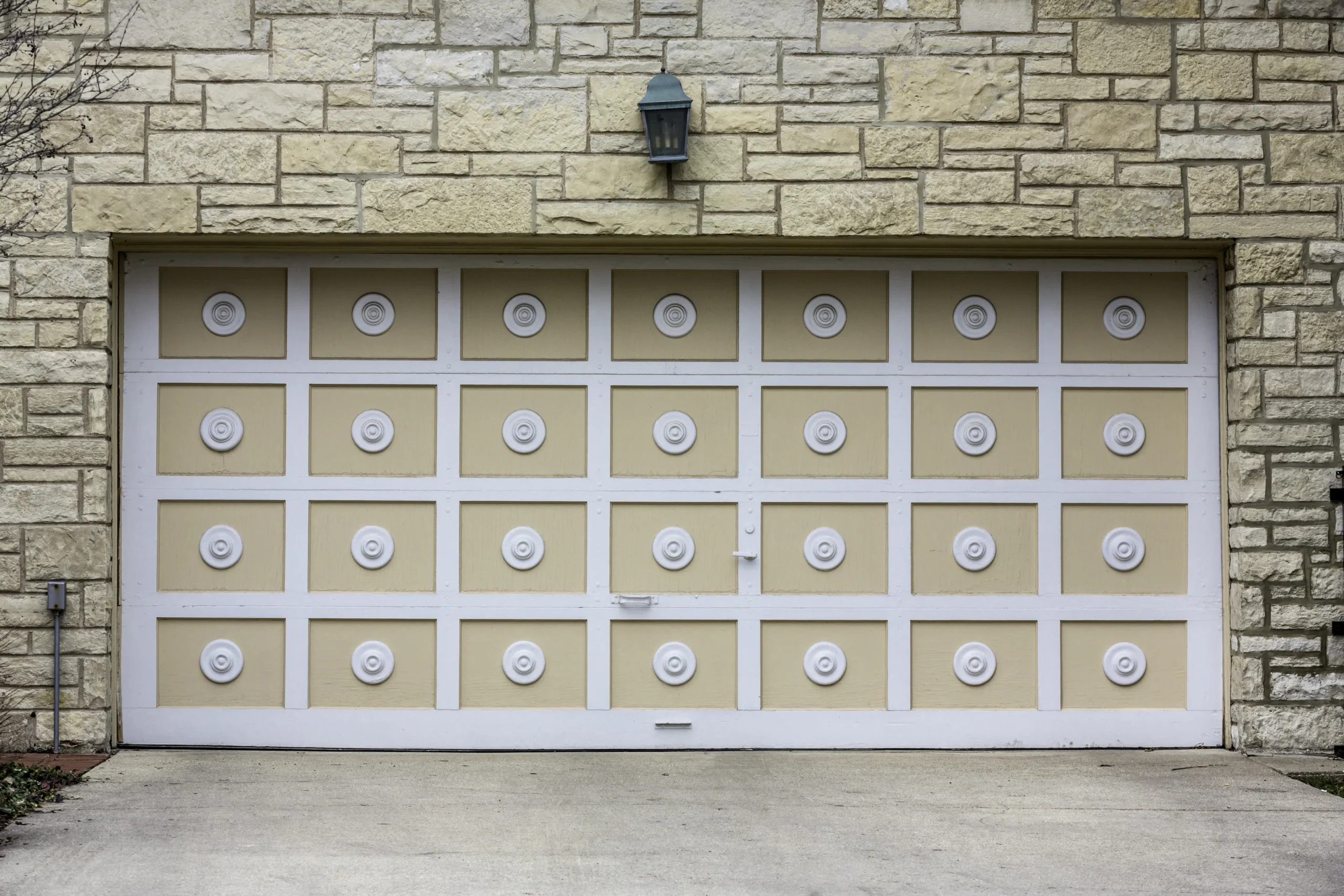 Light-colored garage door with decorative circular panels and a stone wall.