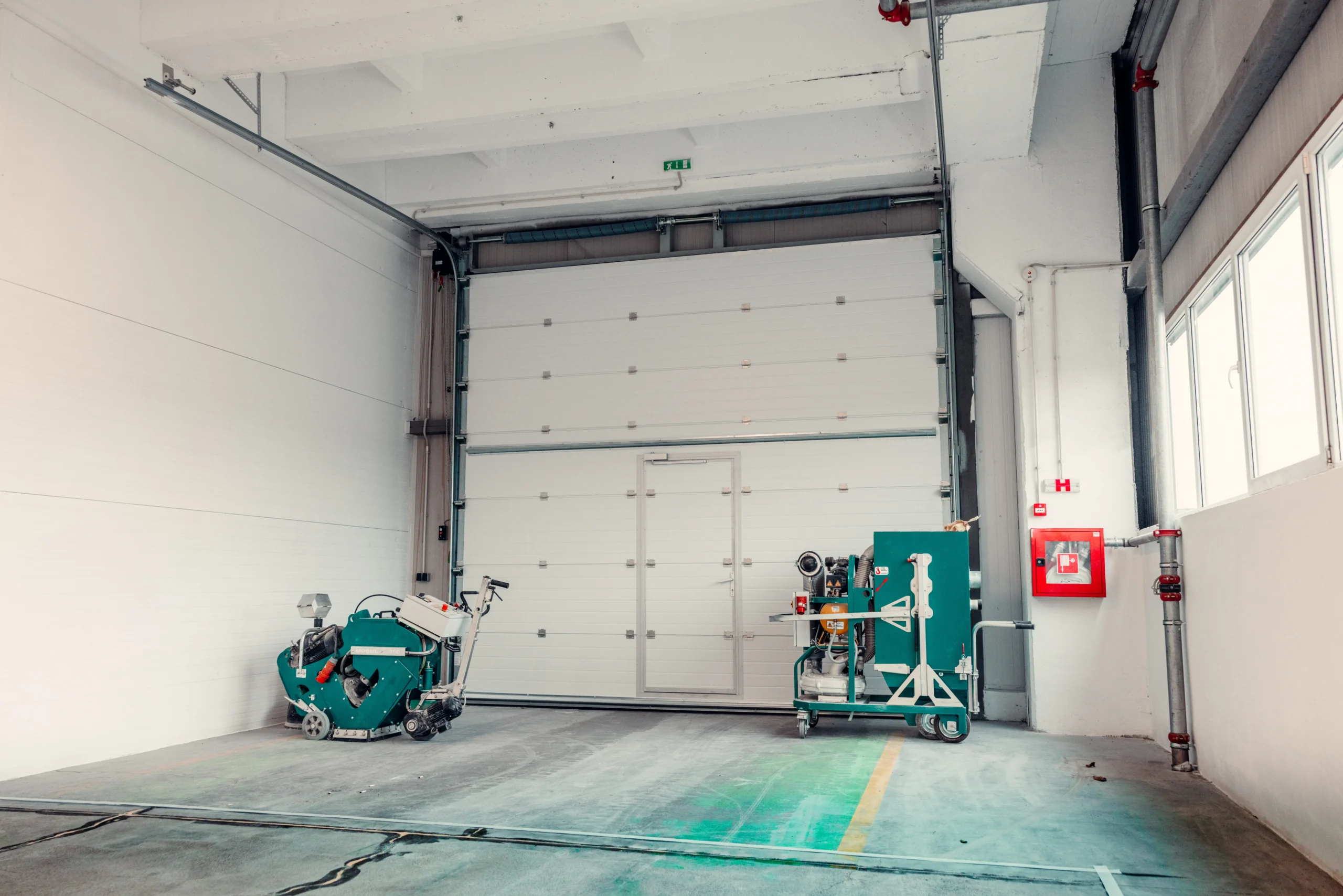 Two green industrial machines in a large, empty white warehouse.
