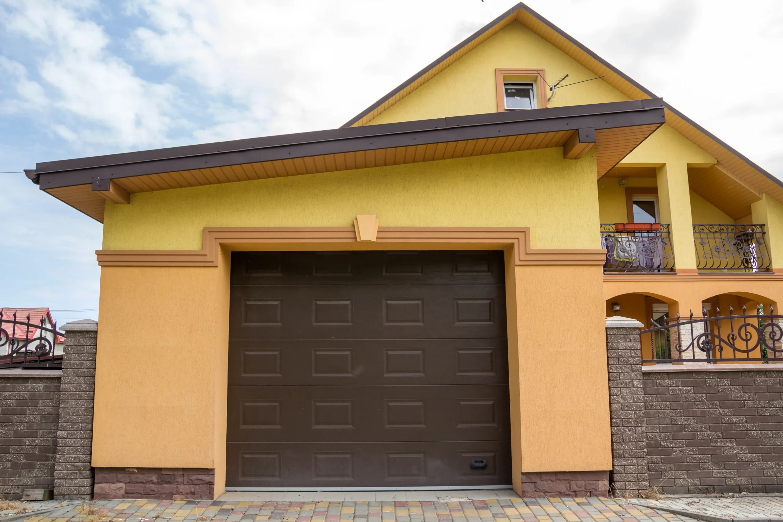 Yellow house with a brown garage door and decorative metal railings