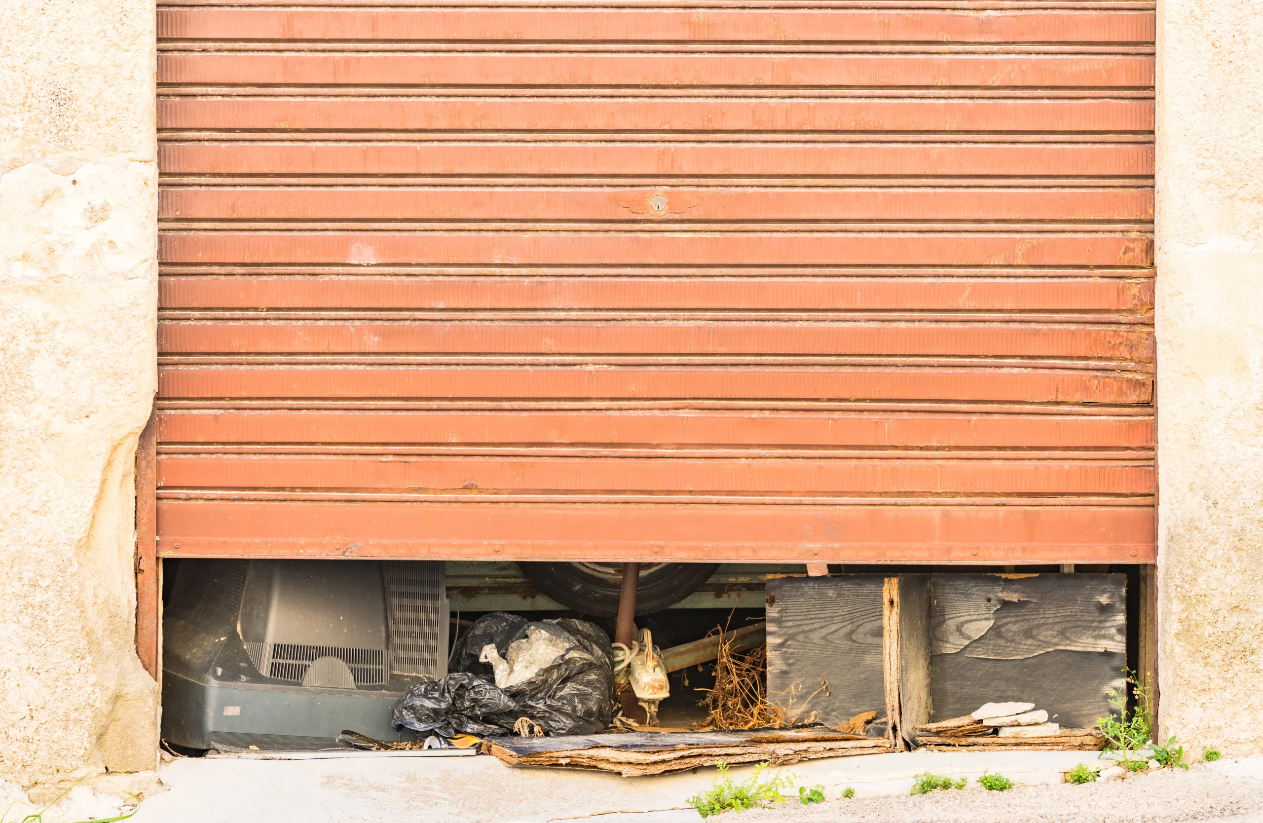 A rusty, closed garage door with debris visible underneath.