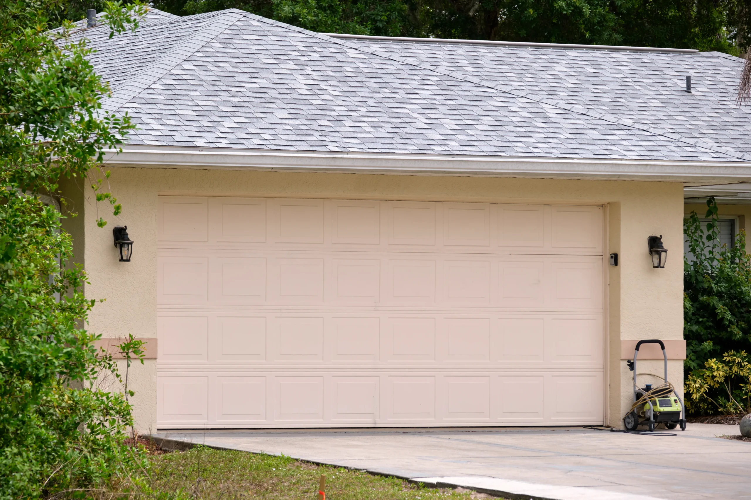 Beige garage door with two black lights on a house with a gray roof