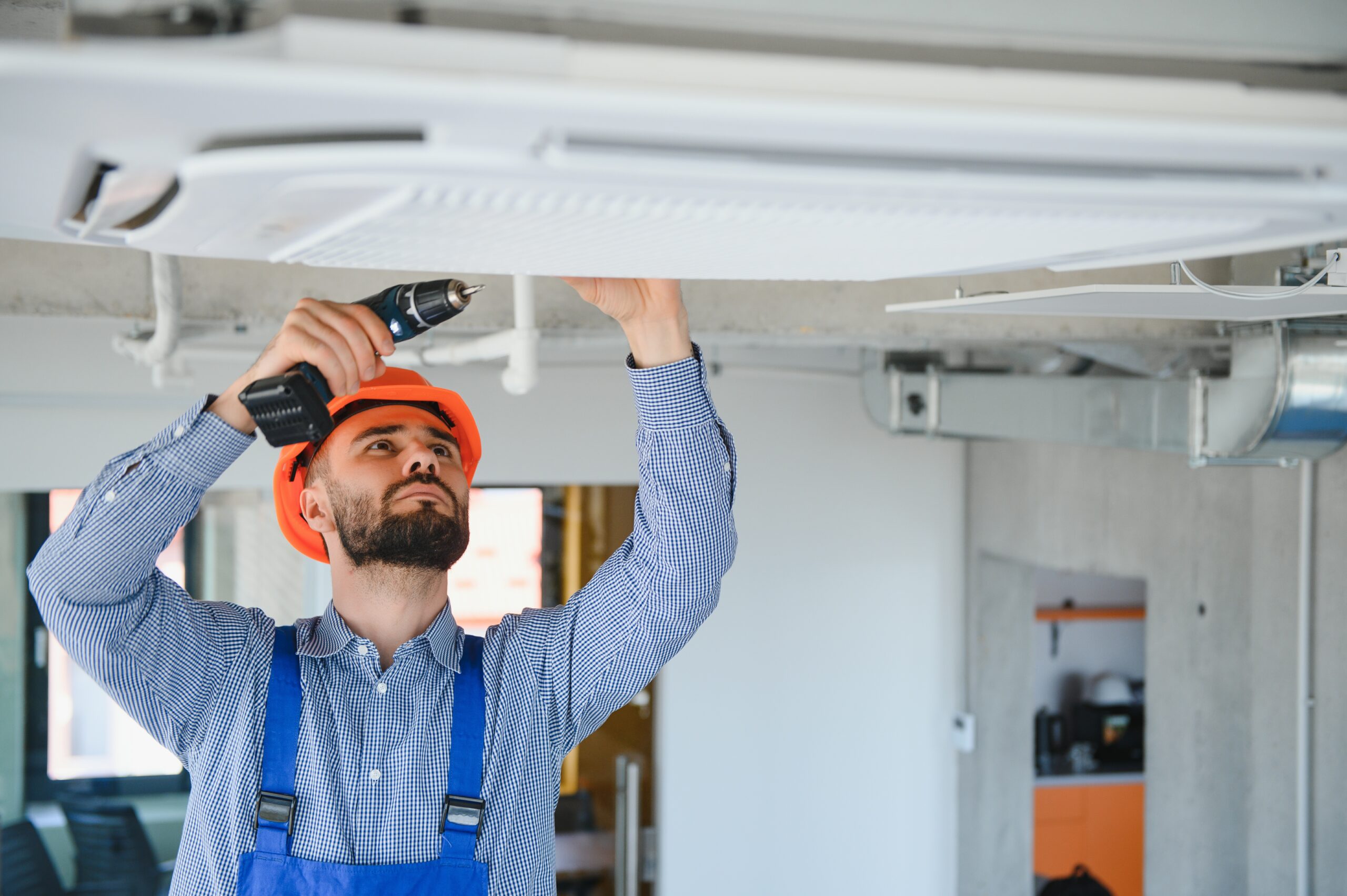 Man in hard hat installing a ceiling unit with a drill