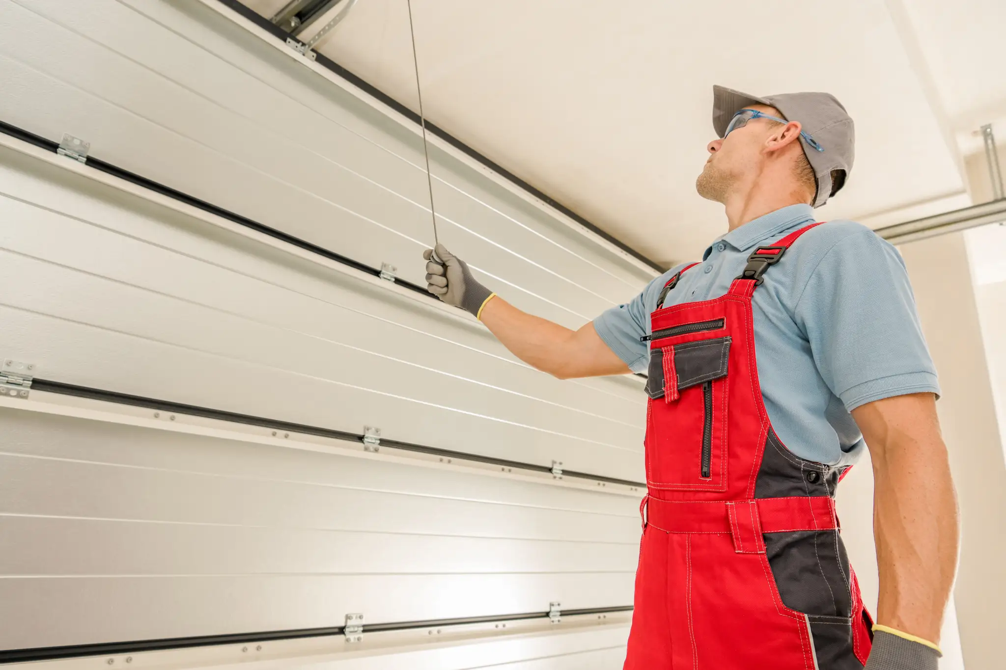 Man in red overalls pulling a cord to open a white garage door.