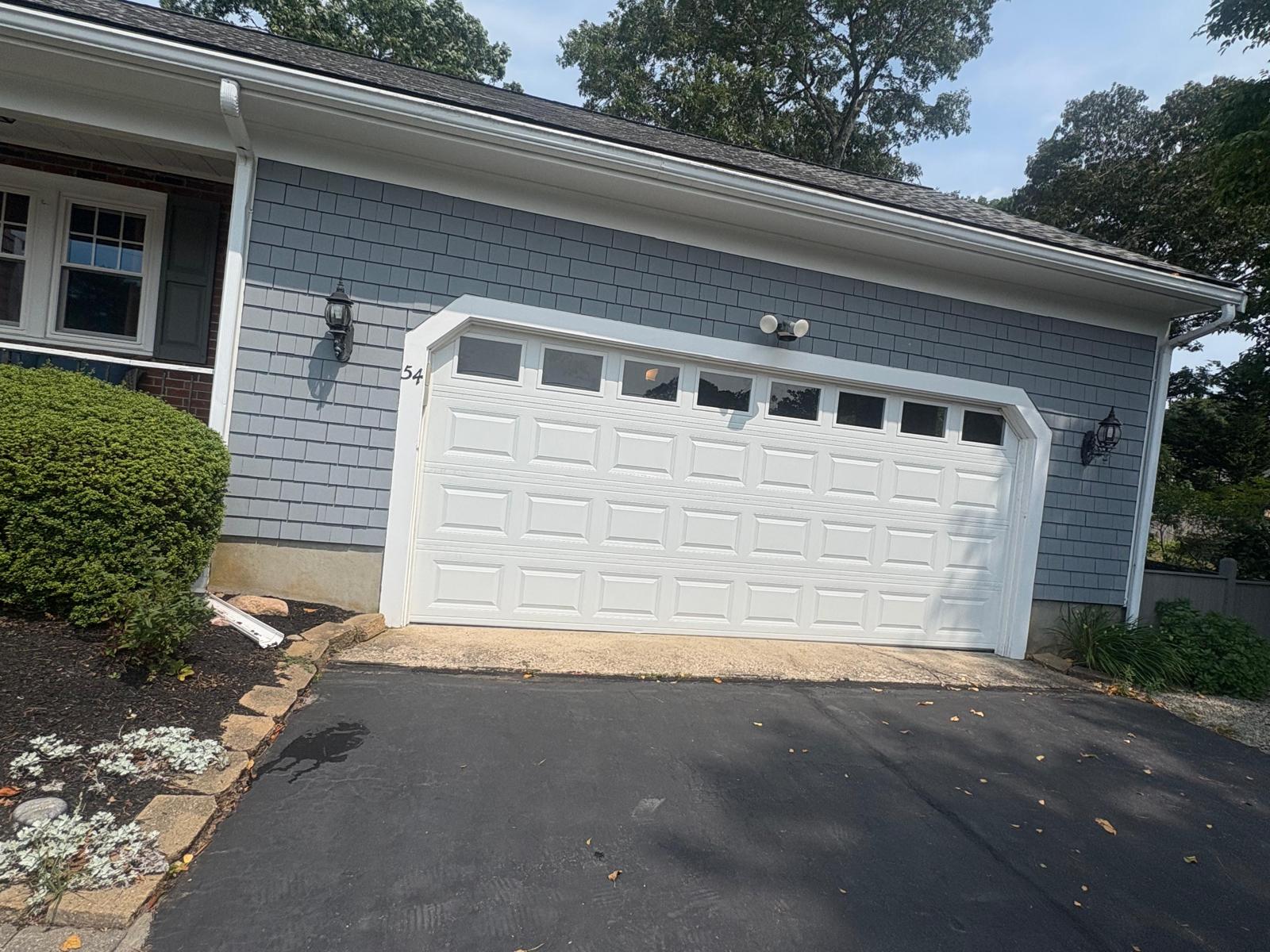 White garage door on a gray house with a black driveway