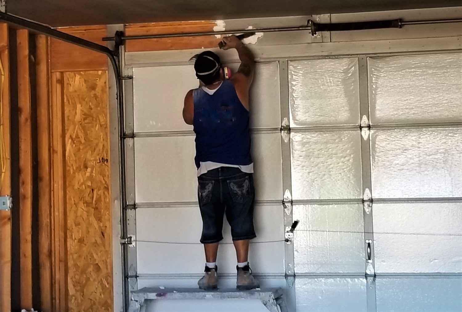 Man on a ladder painting a white garage door.