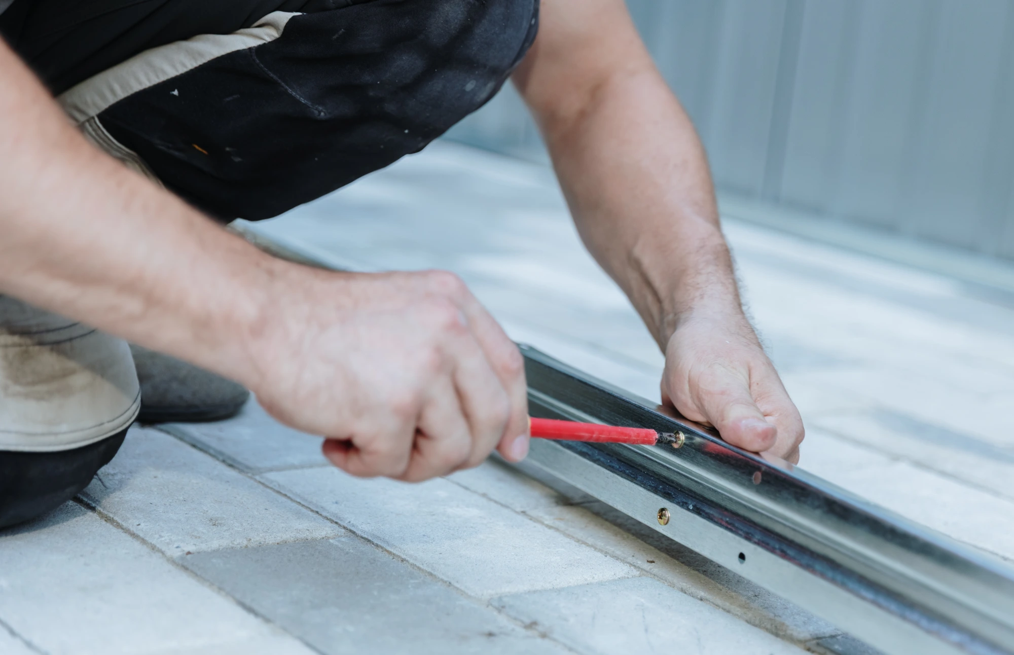 Man installing a metal track on a light-colored tiled floor