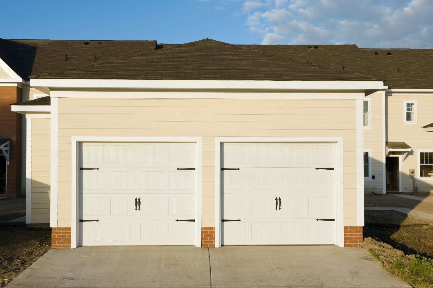 Two white garage doors on a light yellow building under a blue sky.
