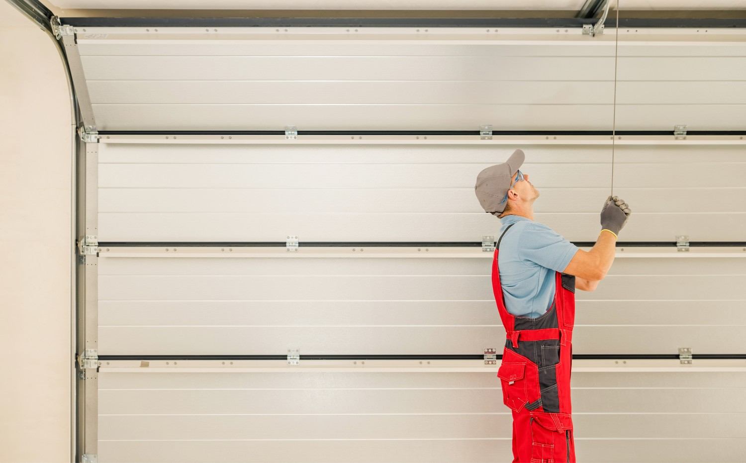 Man in red overalls repairing a white garage door.